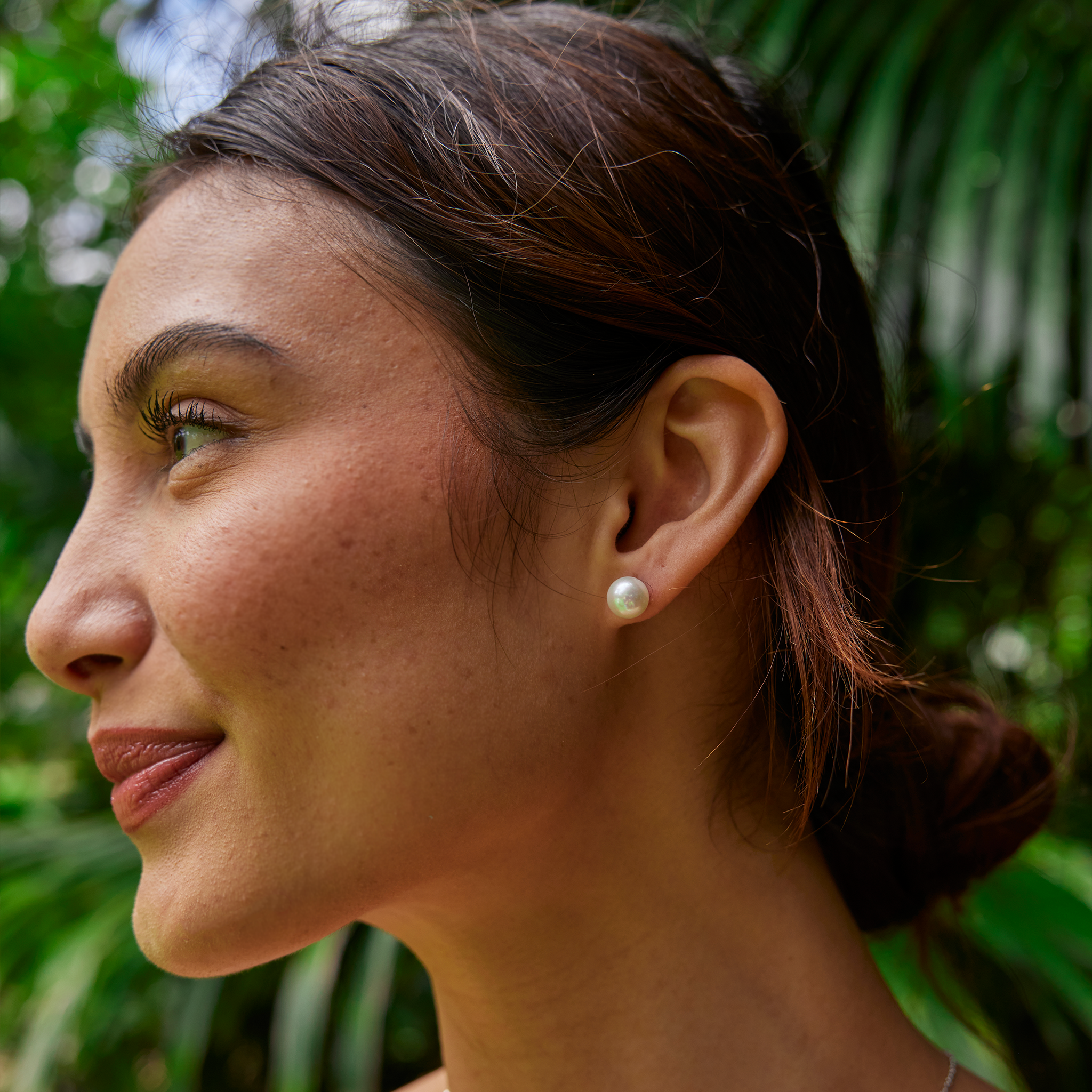 A smiling woman wearing an akoya white pearl earring with a blurry green background.