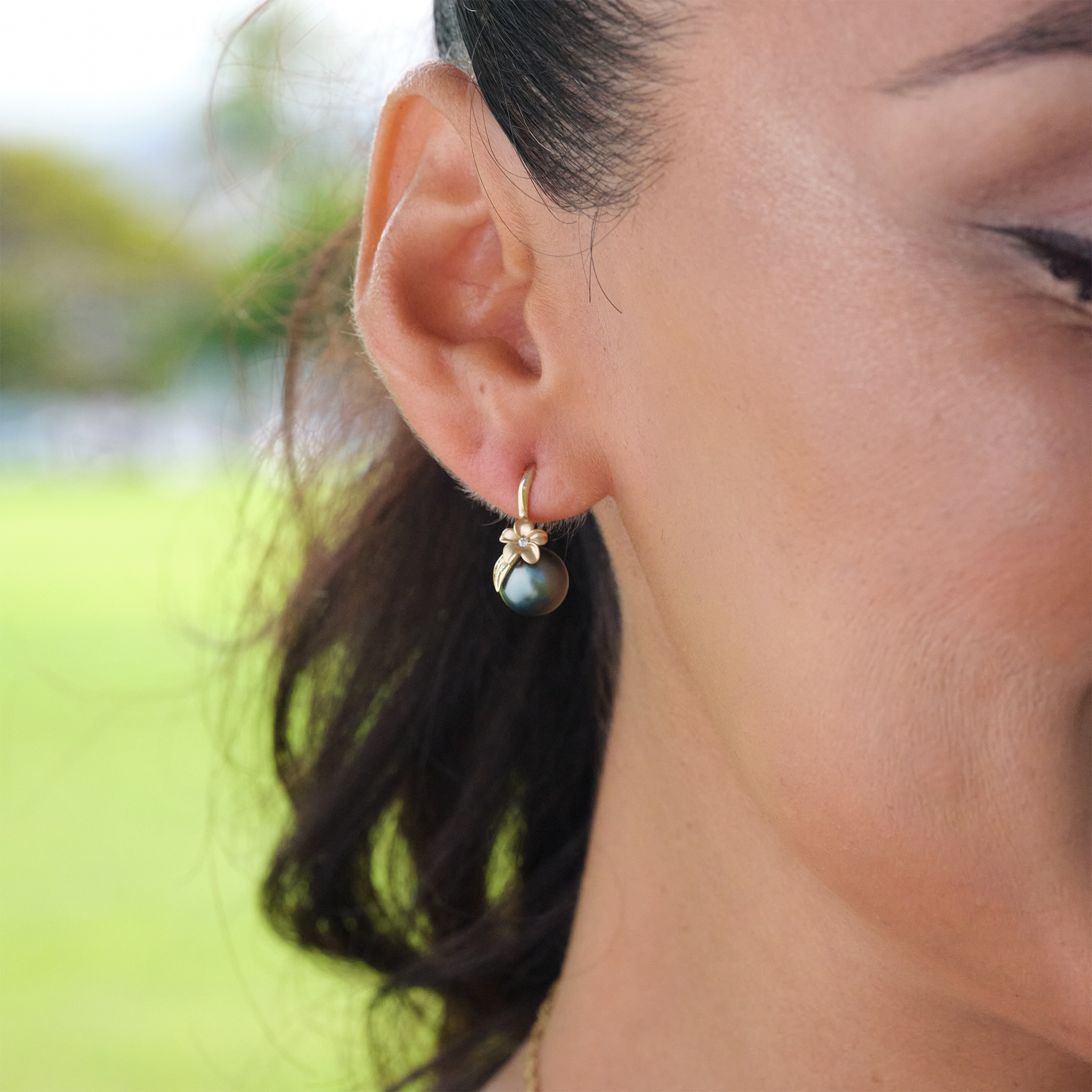 Close-up of a person wearing a plumeria Tahitian black pearl earring in gold with a diamond.