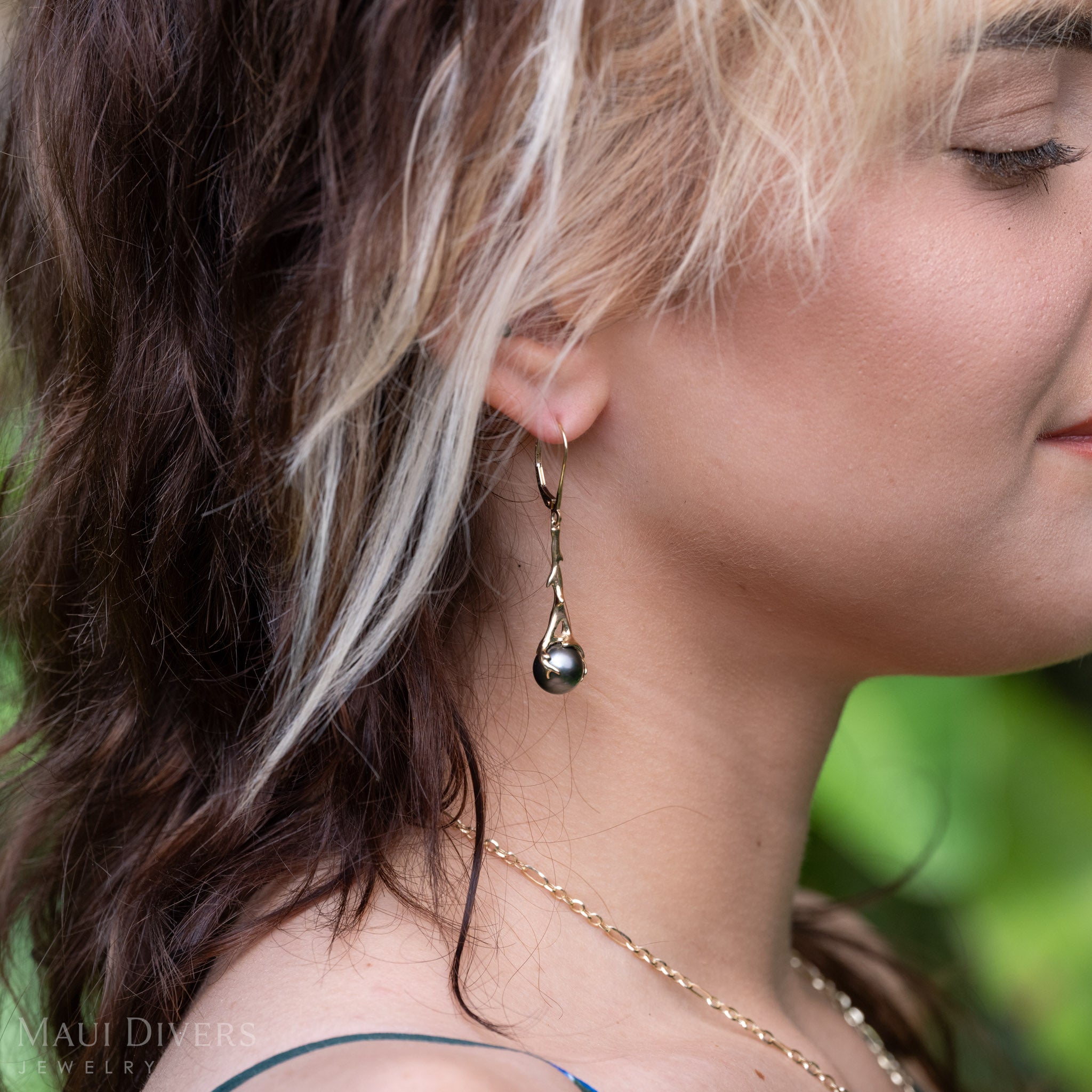 Close-up shot of a woman's ear wearing a Heritage Collection black Coral-branch inspired leverback earrings in solid 14k yellow gold with a Tahitian black pearl