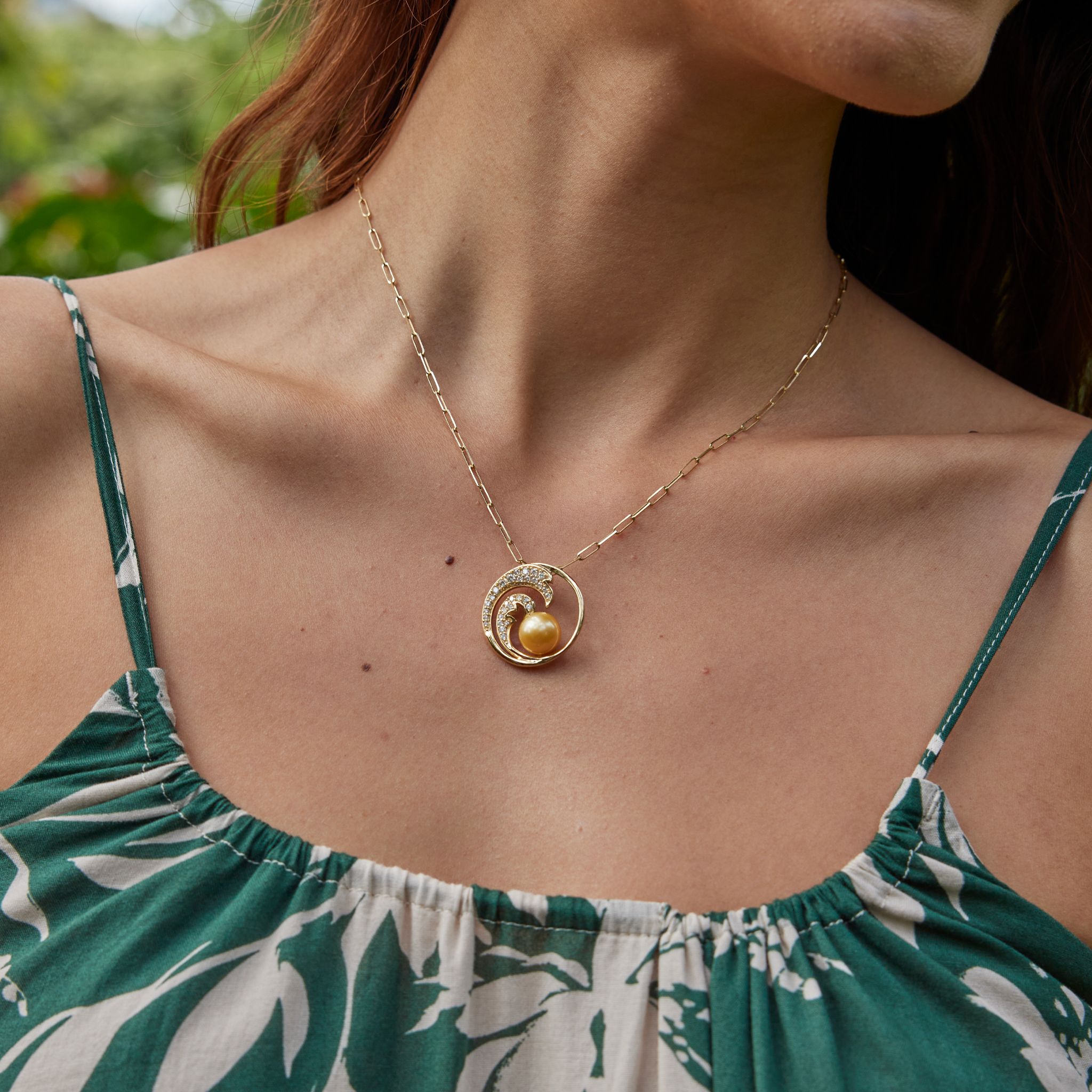 Close up of a person wearing a gold diamond wave South Sea gold pearl pendant on a paperclip chain