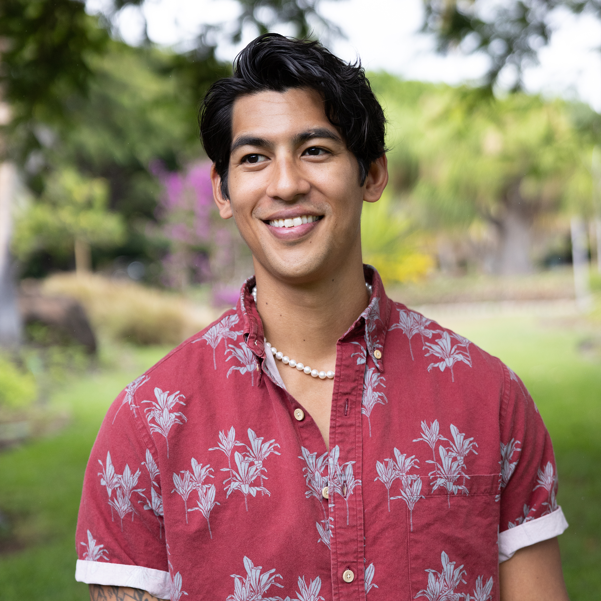 Smiling man in a red Aloha shirt wearing an Akoya white pearl strand necklace against a blurred background
