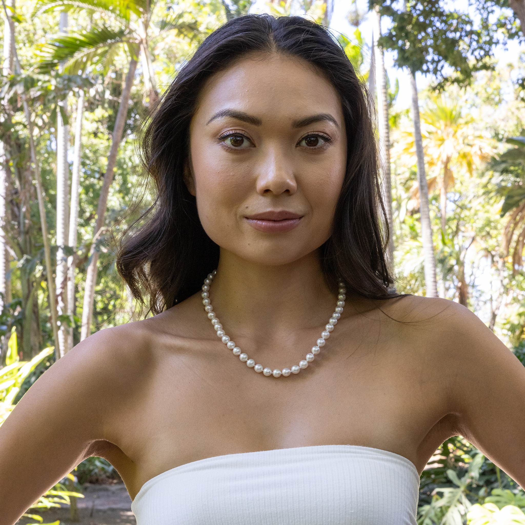 Woman in a white top wearing an Akoya white pearl strand necklace against a blurred background