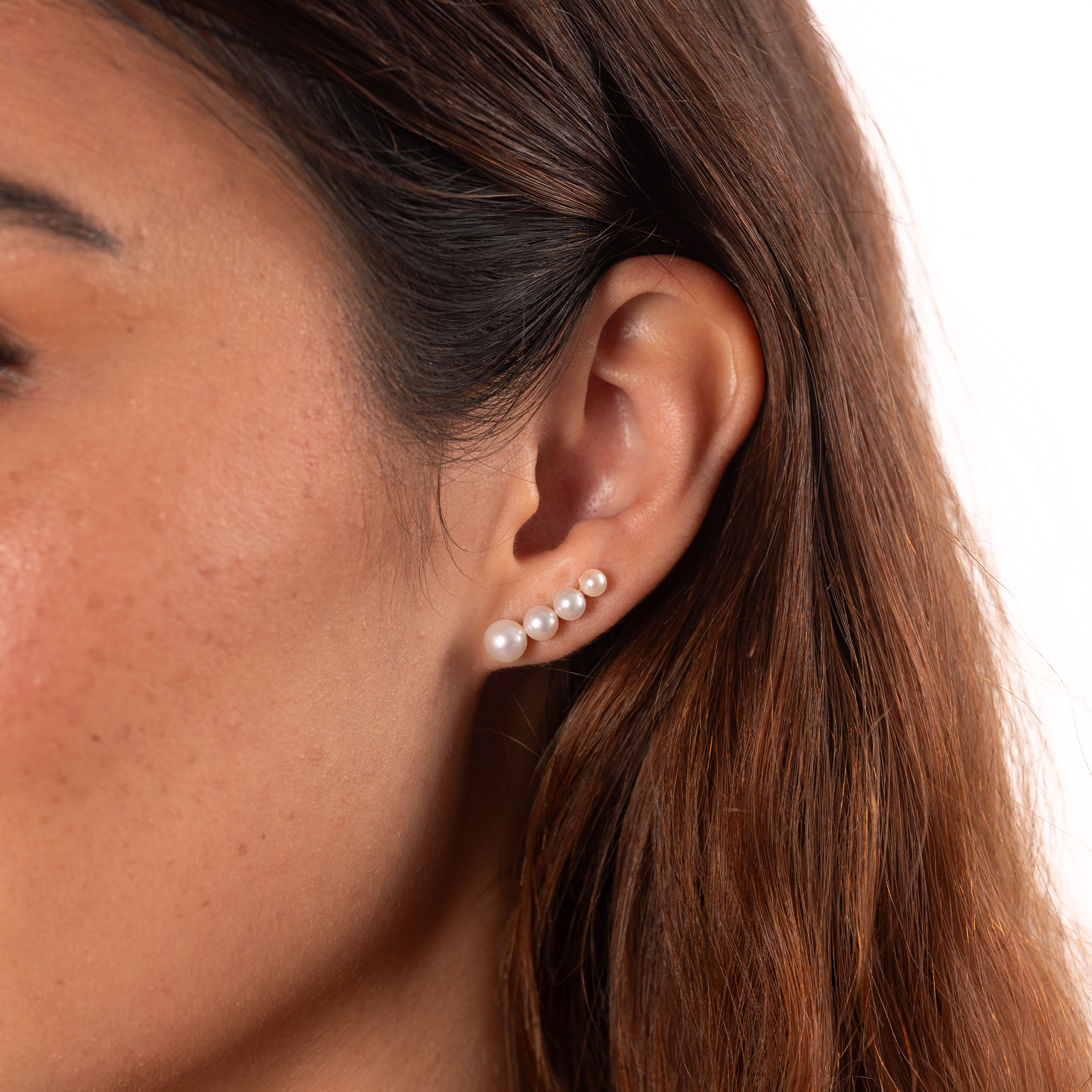 Close-up of a four-pearl gradient earring with Akoya and freshwater white pearls worn on an ear against a white background