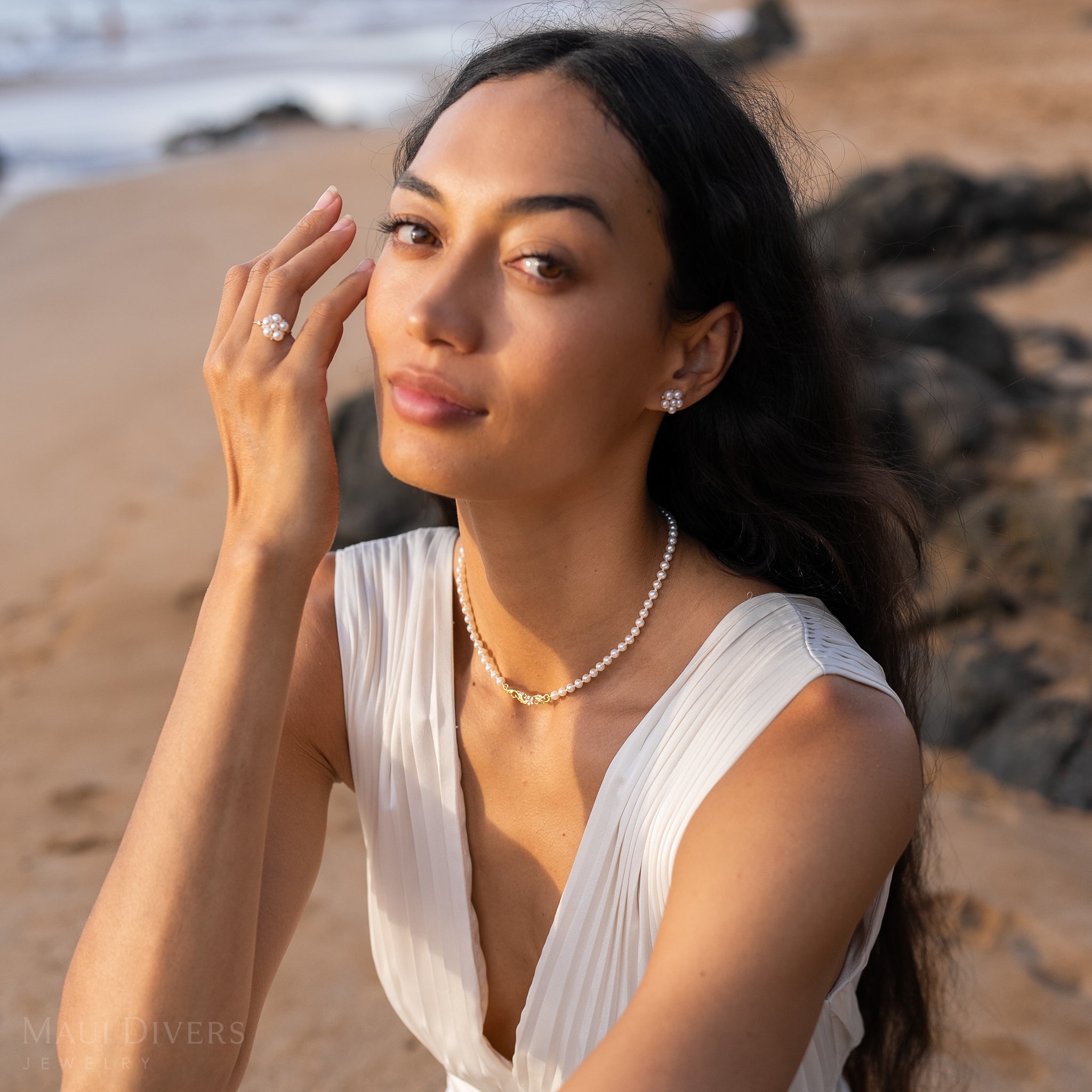 Woman on a beach in a white dress and pearl earrings wearing a Hawaiian Heirloom Plumeria Freshwater White Pearl Necklace