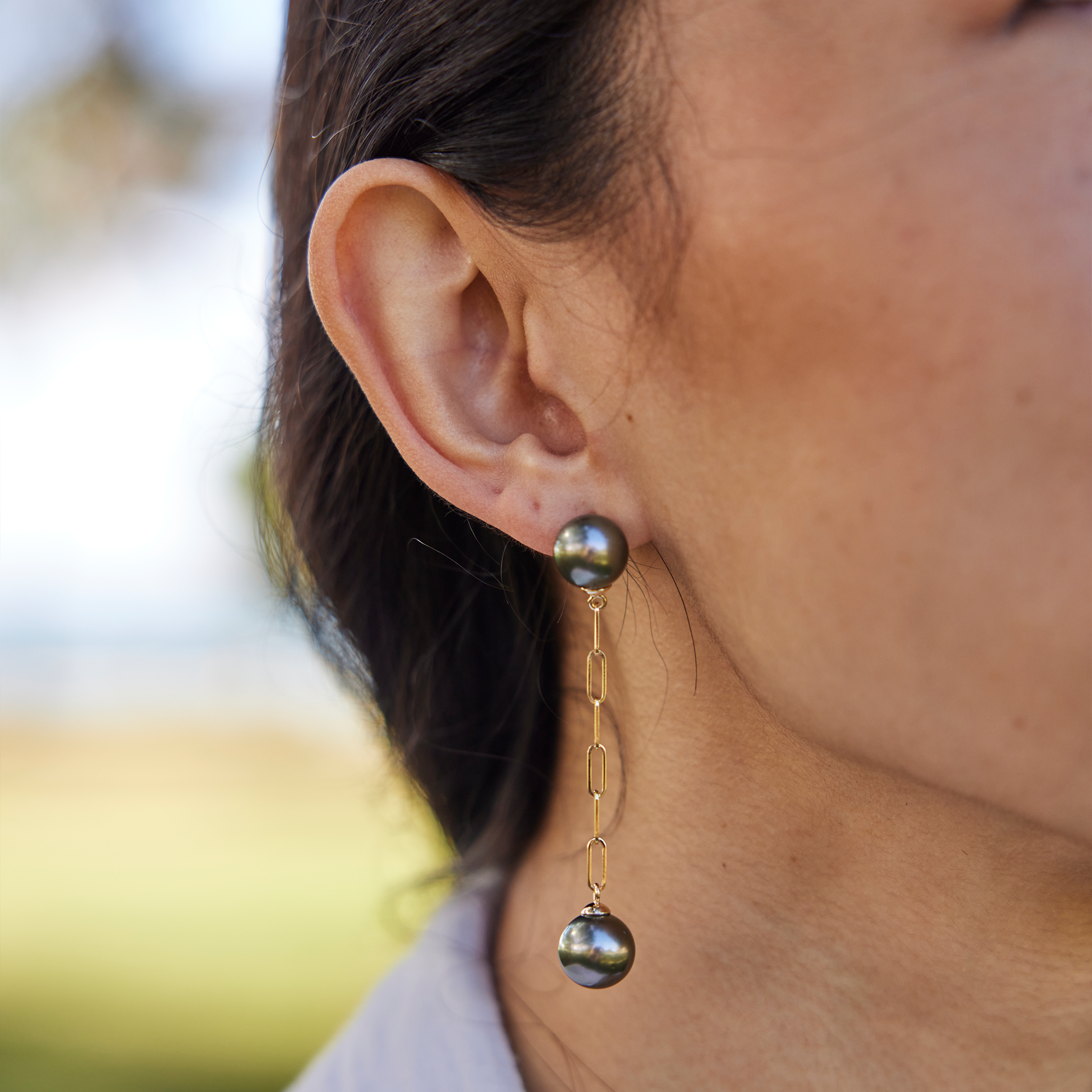 9-10mm Tahitian Black Pearl Paperclip Chain Earrings in 14k Yellow Gold on ear with blurred nature background