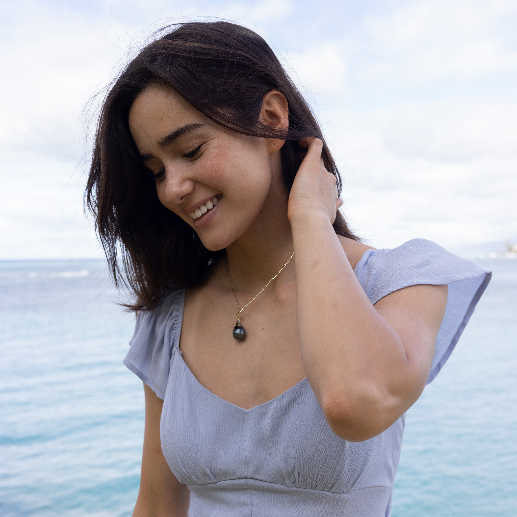 Woman by the ocean wearing a Waterfall Circle 14-17mm Tahitian Black Pearl Pendant in Gold