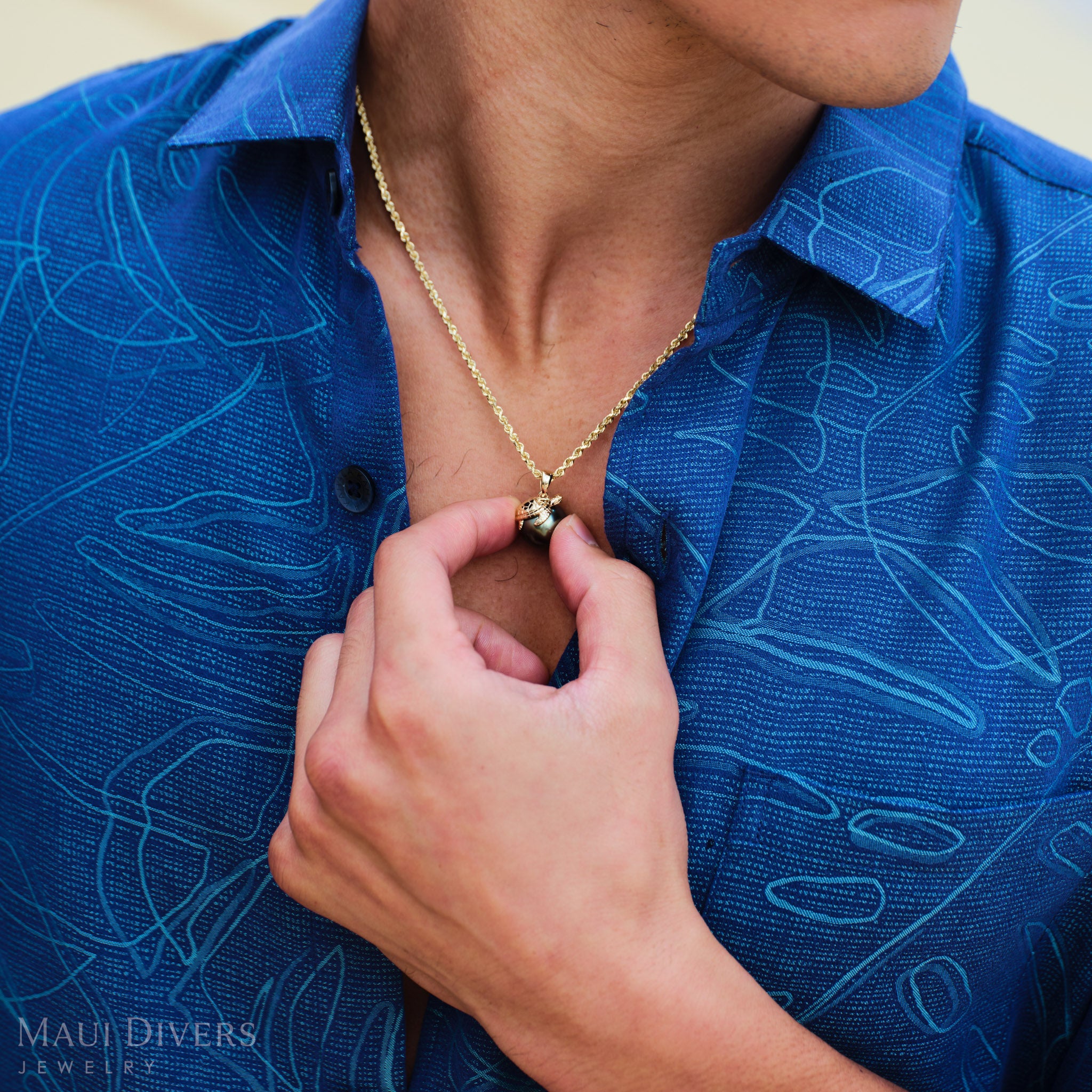 Man wearing a blue patterned shirt and a Honu 13-14mm Tahitian Black Pearl Pendant in Gold