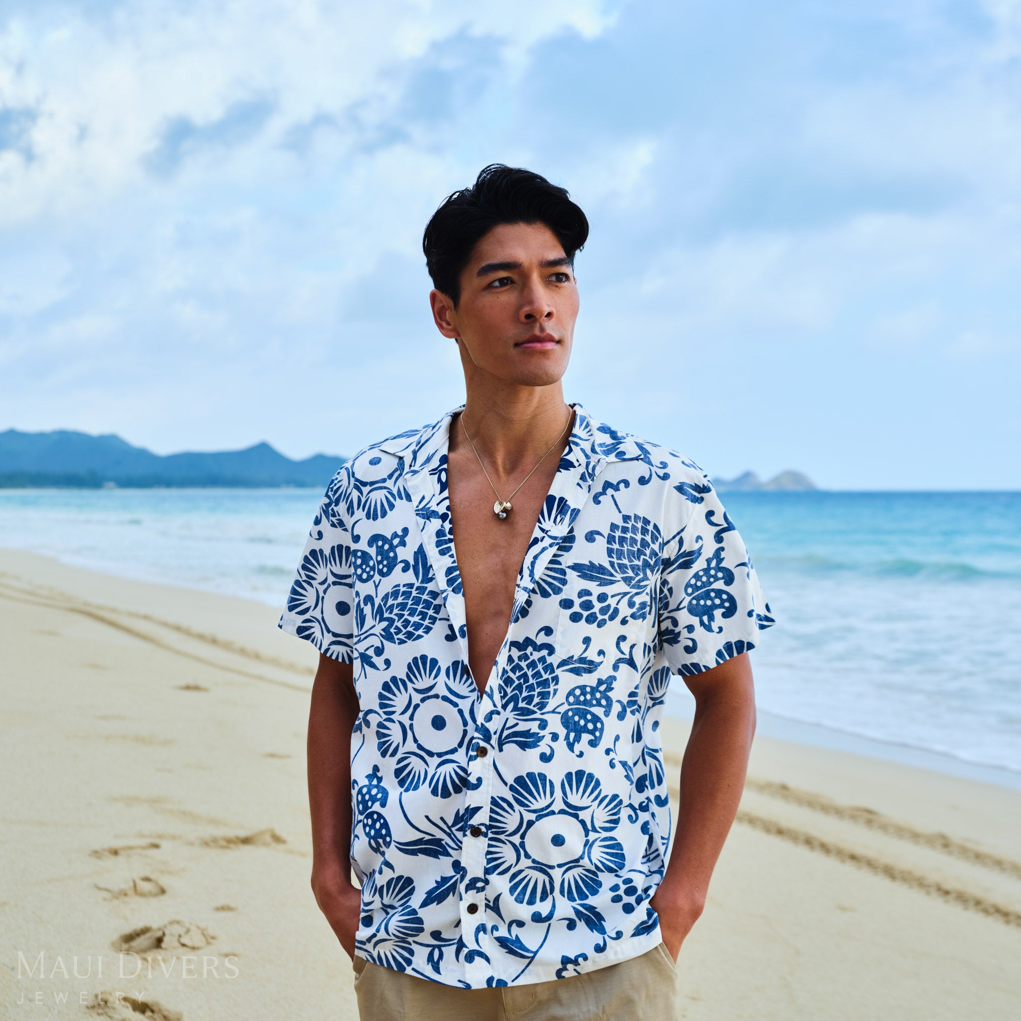 Man wearing a blue and white patterned shirt with a Kalo 12-15mm Circle Tahitian Black Pearl Pendant in Gold on a beach
