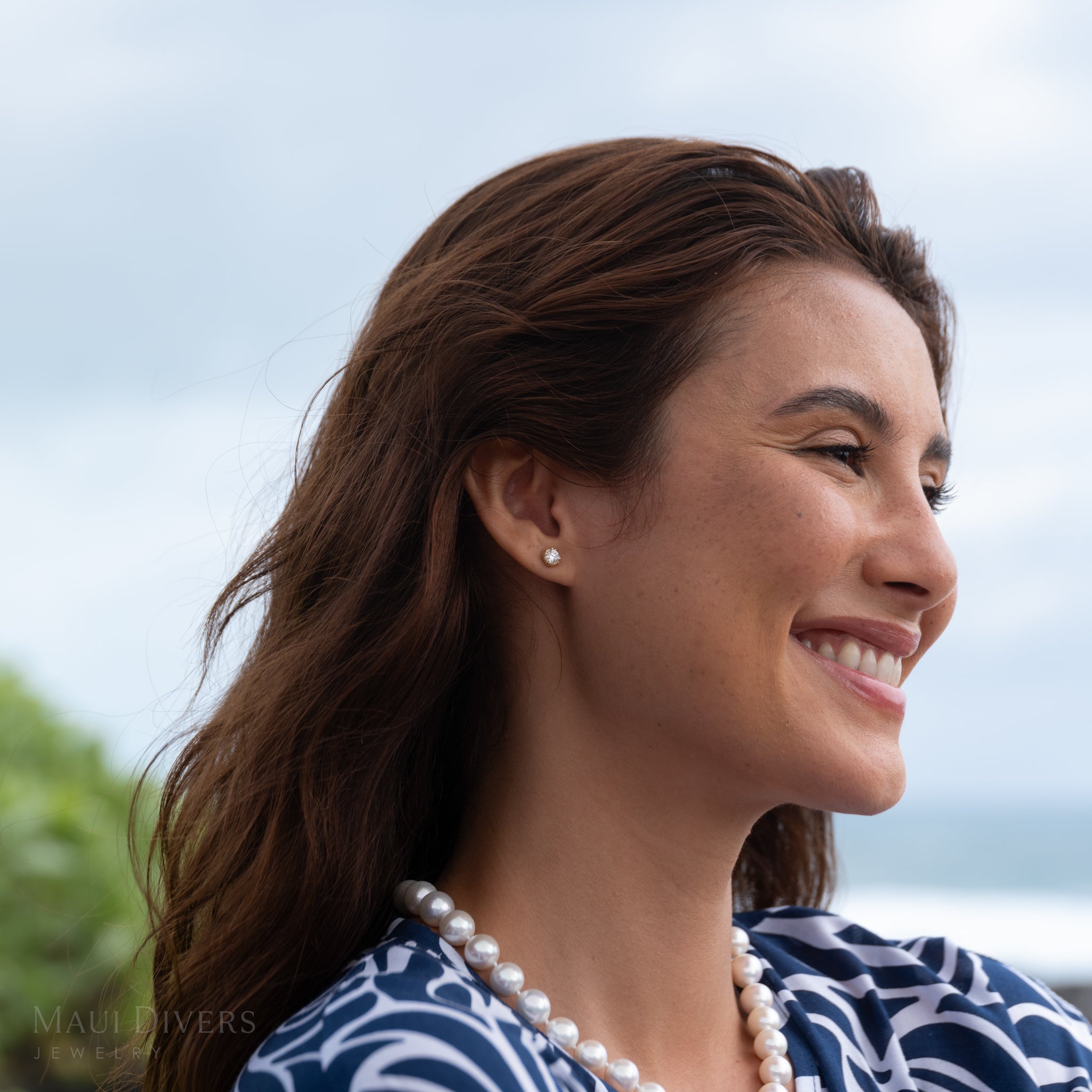 Woman wearing a Hidden Hawaiʻi Maile Lab Grown Diamond Earring and white pearl necklace with a blurred natural background