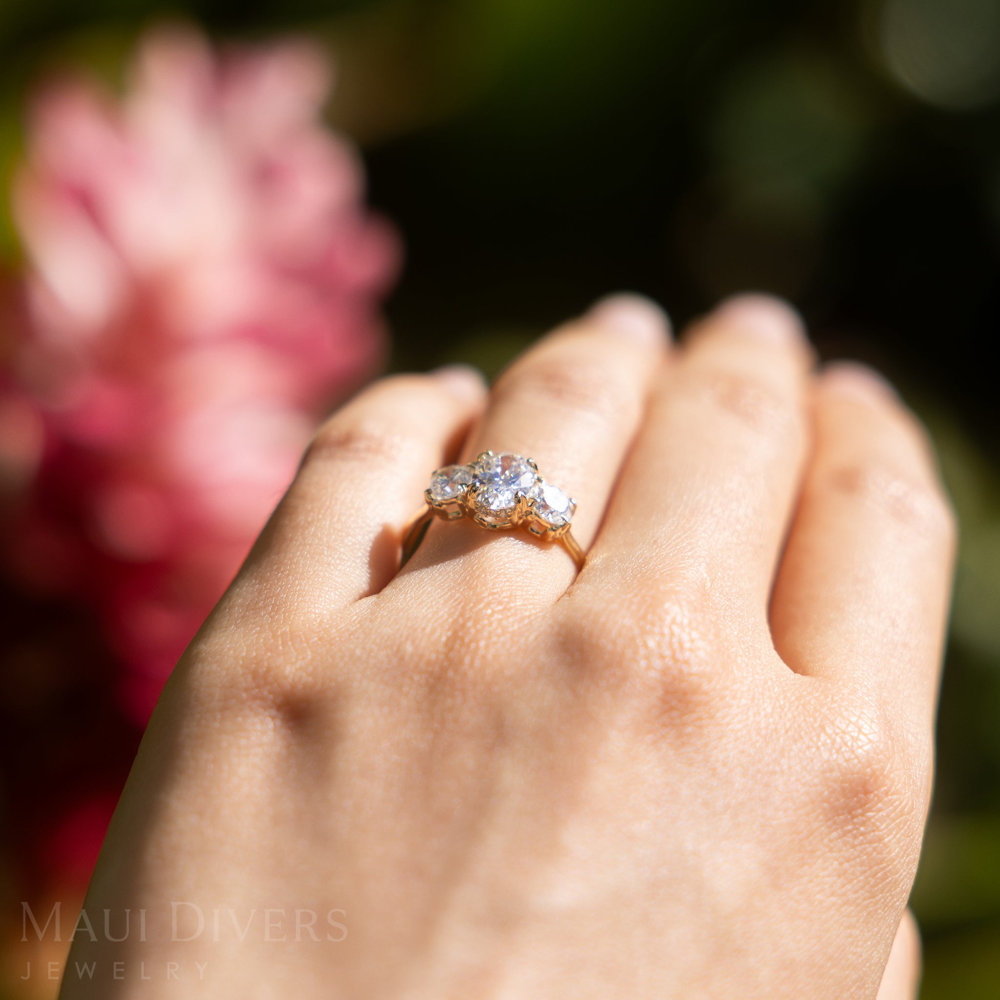 Hand wearing a lab-grown diamond ring in 14k yellow gold with a blurred floral background