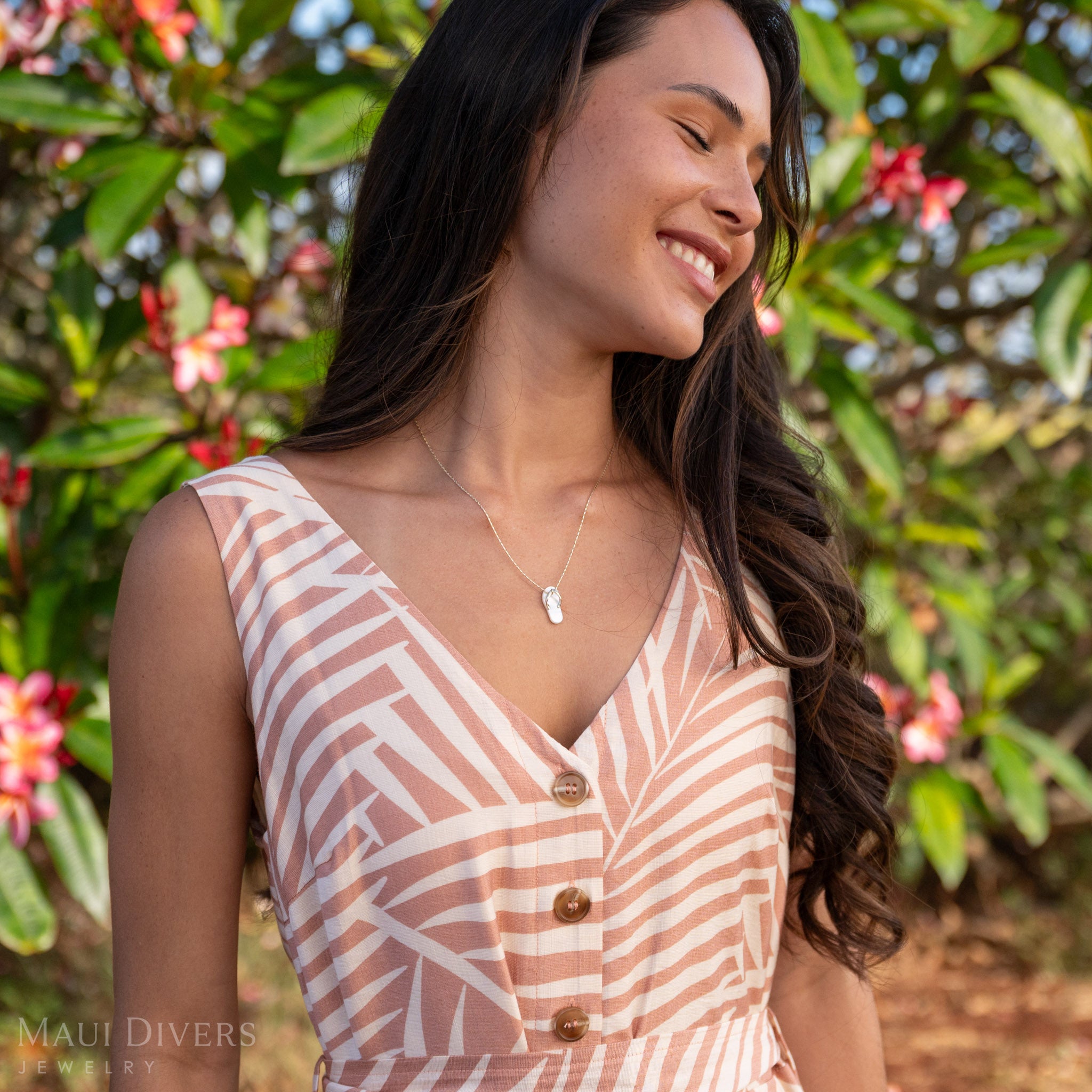 Woman tilting her head to the side and smiling wearing a White Mother of Pearl Slipper Pendant with 14k Gold details with a pink and green nature background.