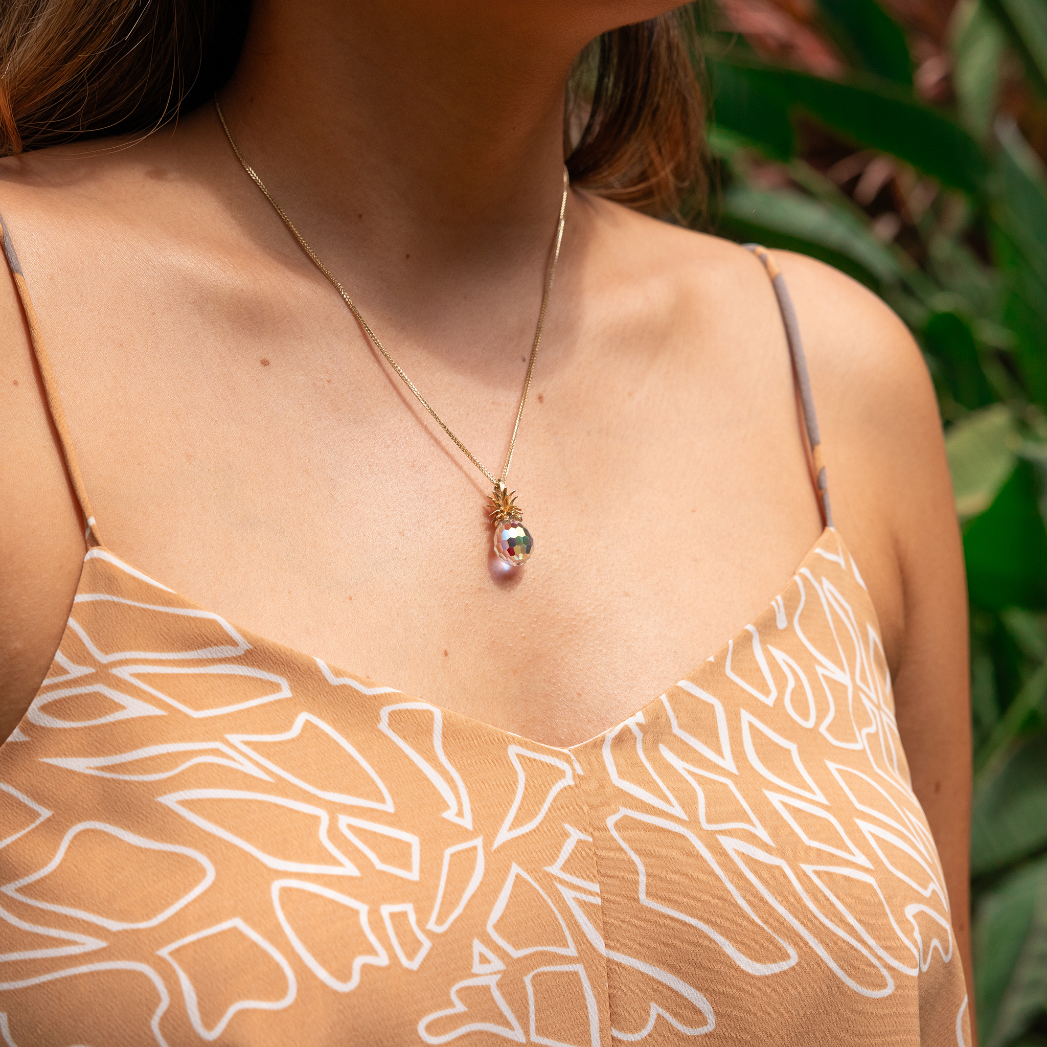 Clost up of woman wearing Crystal Pineapple Pendant with Gold crown among greenery