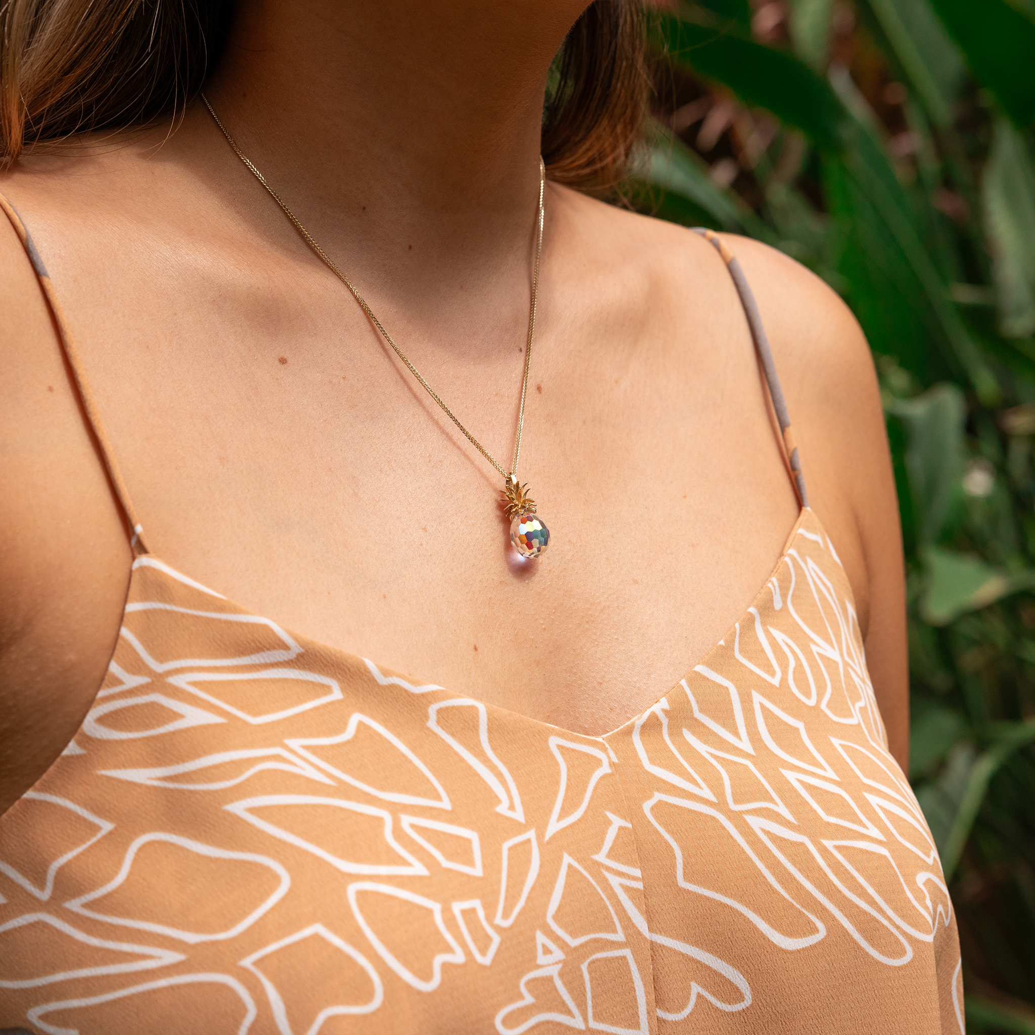 Clost up of woman wearing Crystal Pineapple Pendant with Gold crown among greenery