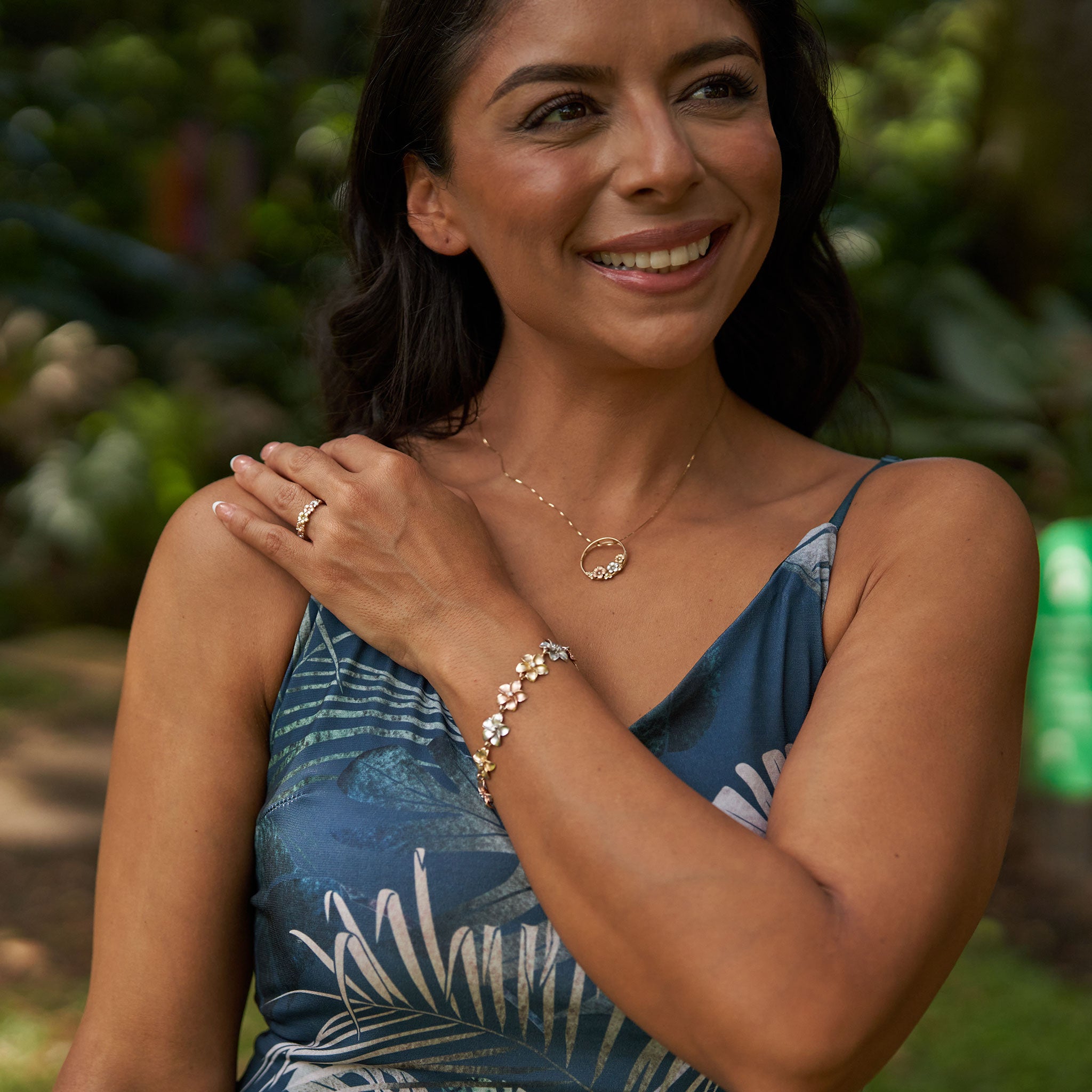 Woman in a garden wearing Tri-Color Gold Plumeria Ring, Pendant and Bracelet with Diamonds