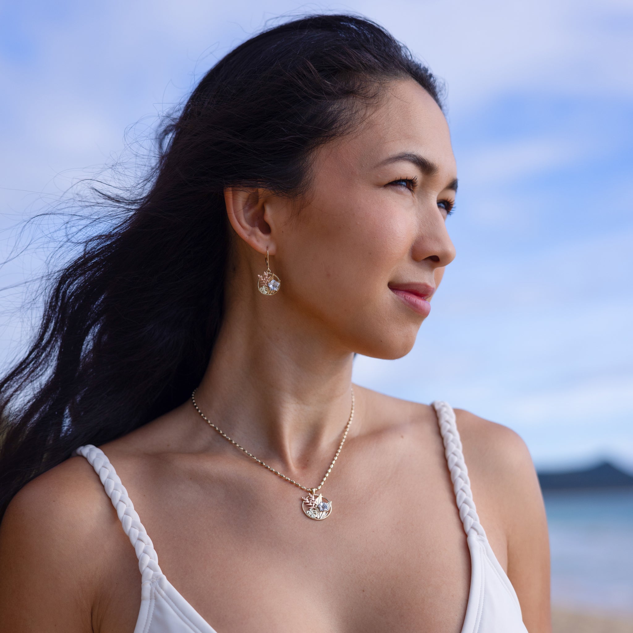 Woman at the beach wearing Hawaiian Gardens Hibiscus Earrings and Pendant in Four Tone Gold with Diamonds