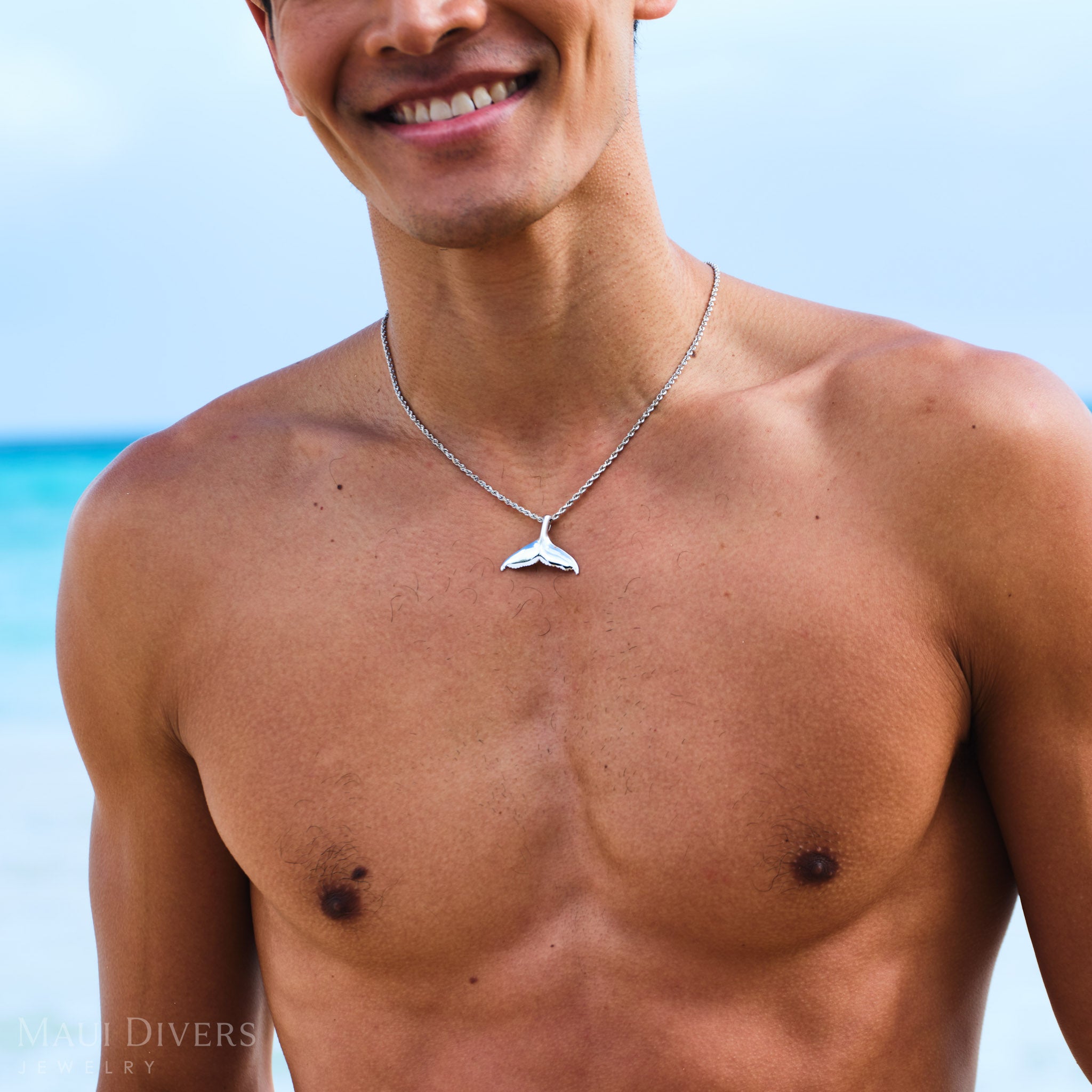 Man wearing a rope chain with a white gold whale tail pendant on a beach