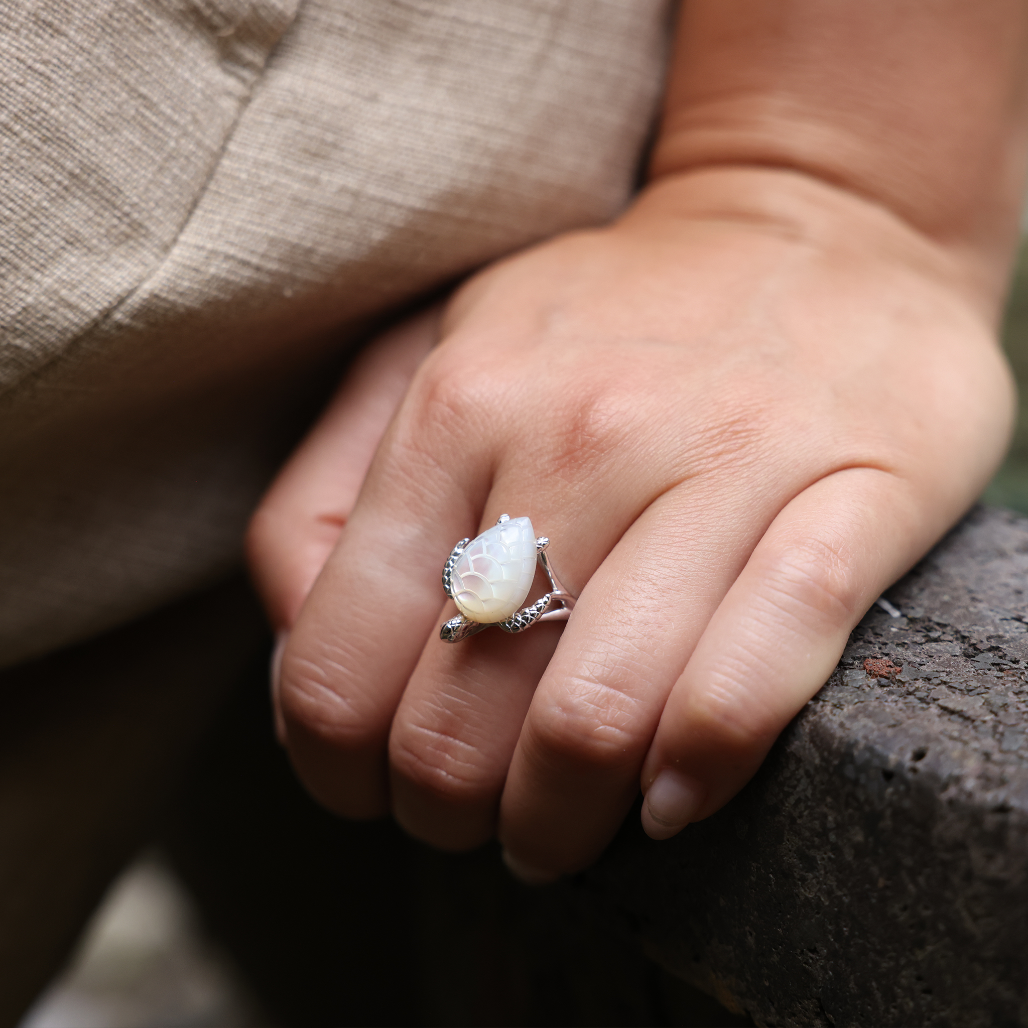 Close up of Honu Mother of Pearl Ring in White Gold on hand leaning on rock