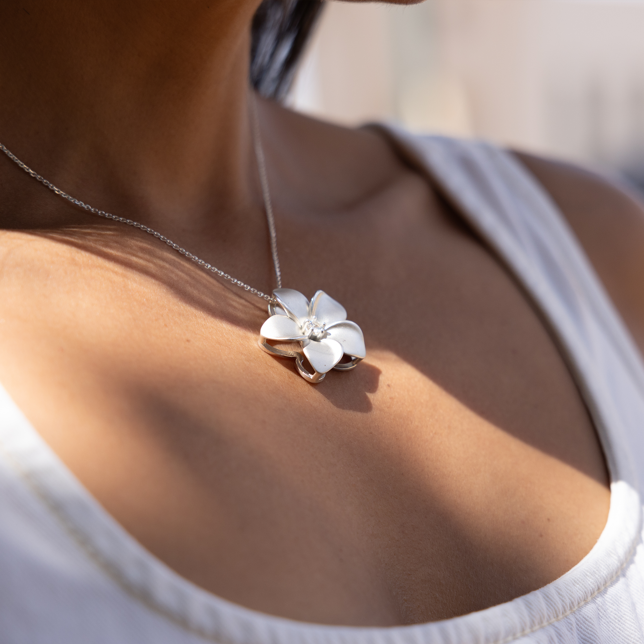Close up of Plumeria White Sapphire Necklace in Sterling Silver on a woman's chest