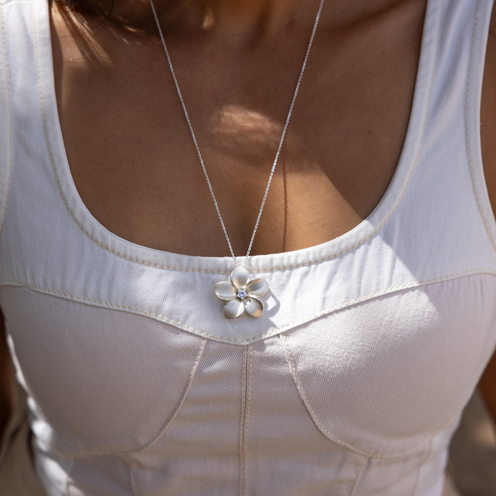 Close up of a Plumeria White Sapphire Necklace in Sterling Silver on a woman's chest