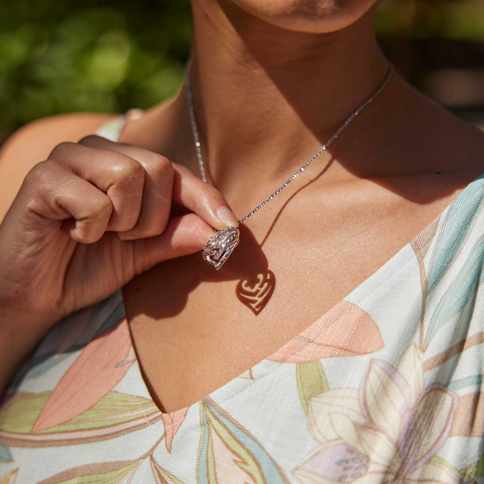 Woman wearing an Aloha Heart Plumeria Pendant in Sterling Silver to cast a shadow spelling Aloha
