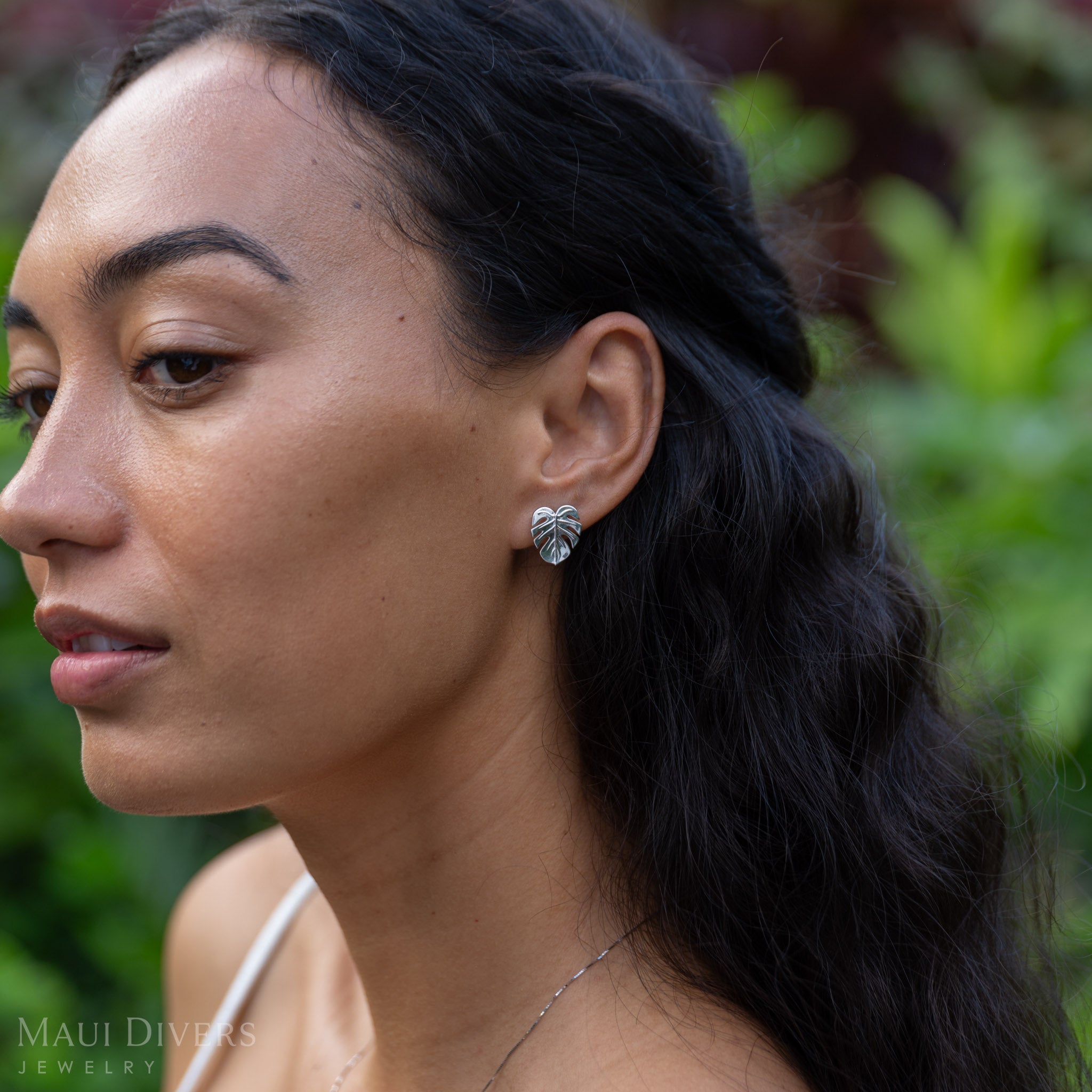 Woman wearing a Monstera Earring in Sterling Silver with a blurred green background