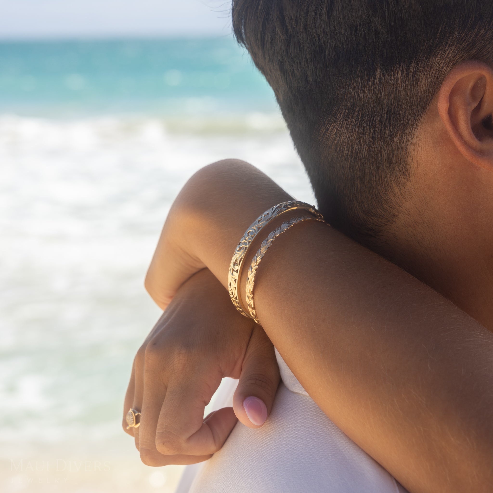 Arms hugging a man on a beach with Hawaiian Heirloom Plumeria Hinge Bracelet in Gold
