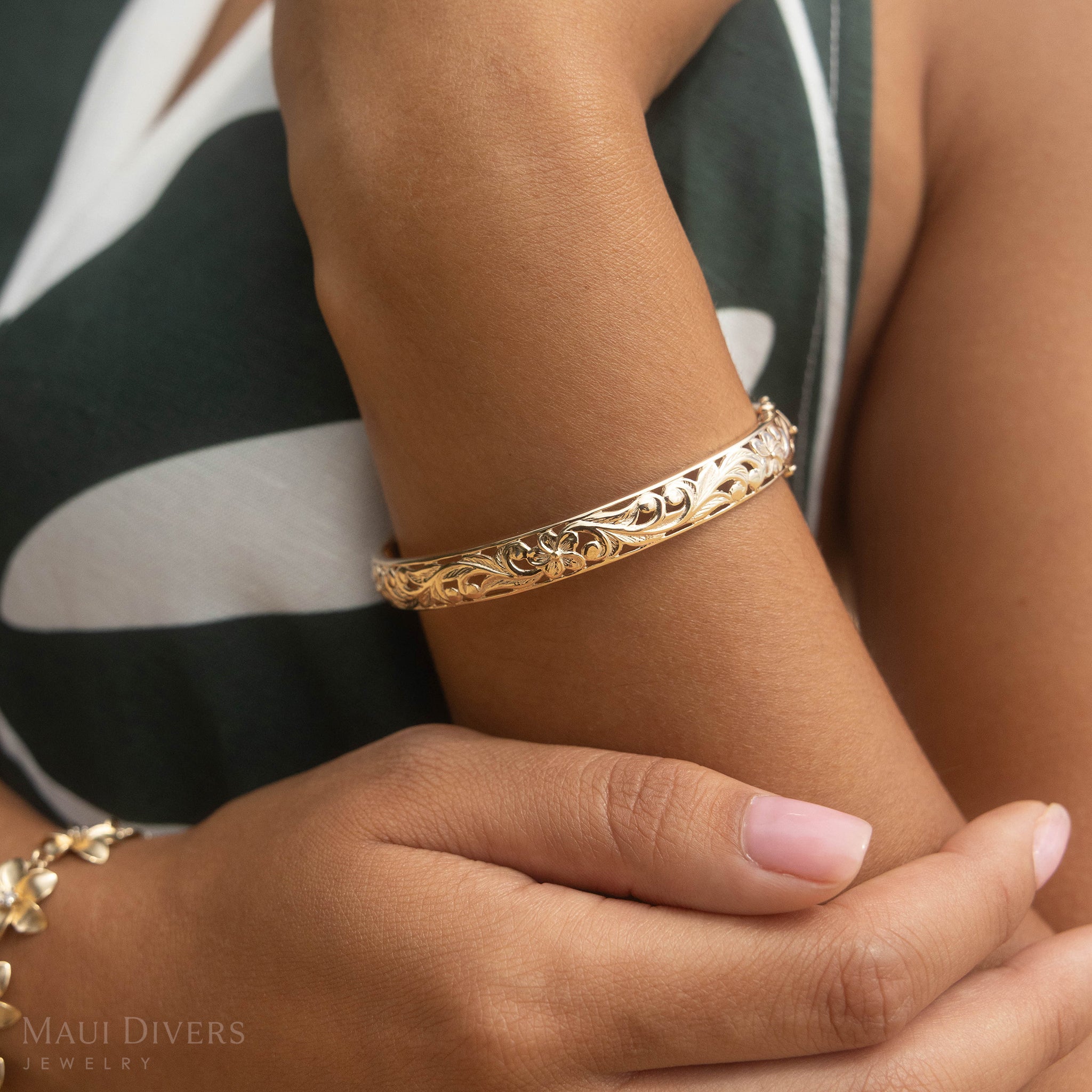 Hawaiian Heirloom Plumeria Hinge Bracelet in Gold on a wrist with a green dress behind