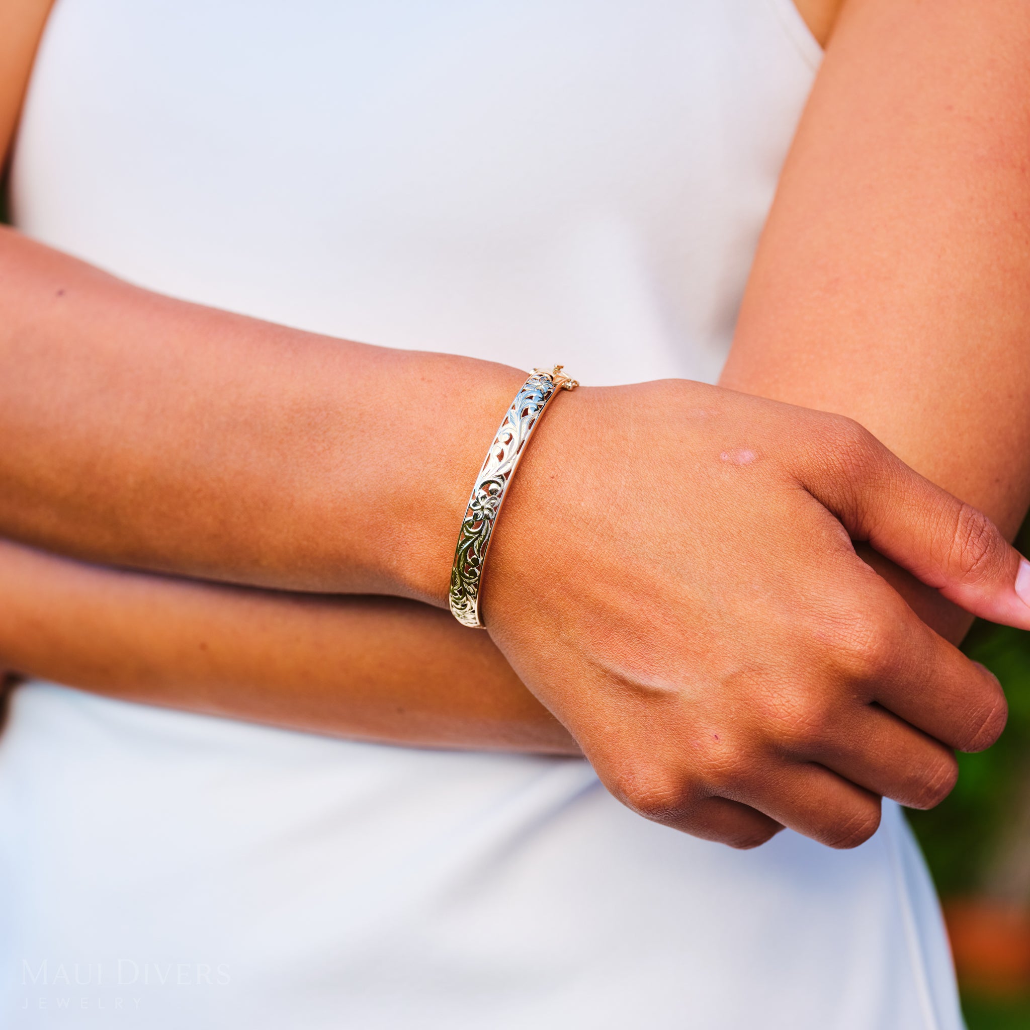 Close-up of a person's arm wearing a Hawaiian Heirloom Plumeria Hinge Bracelet on a white dress