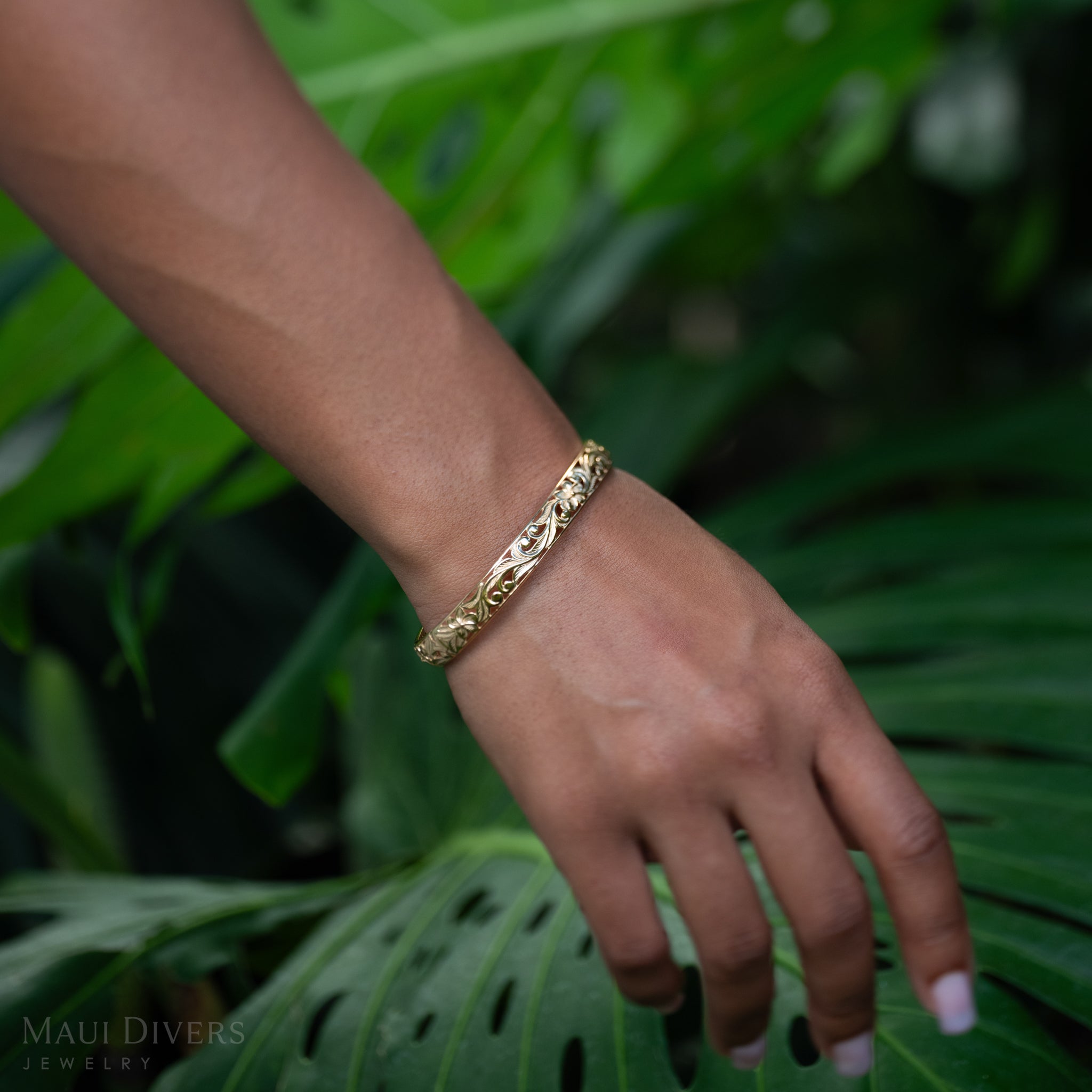 Hawaiian Heirloom Plumeria Hinge Bracelet in Gold on a wrist with a green leafy background