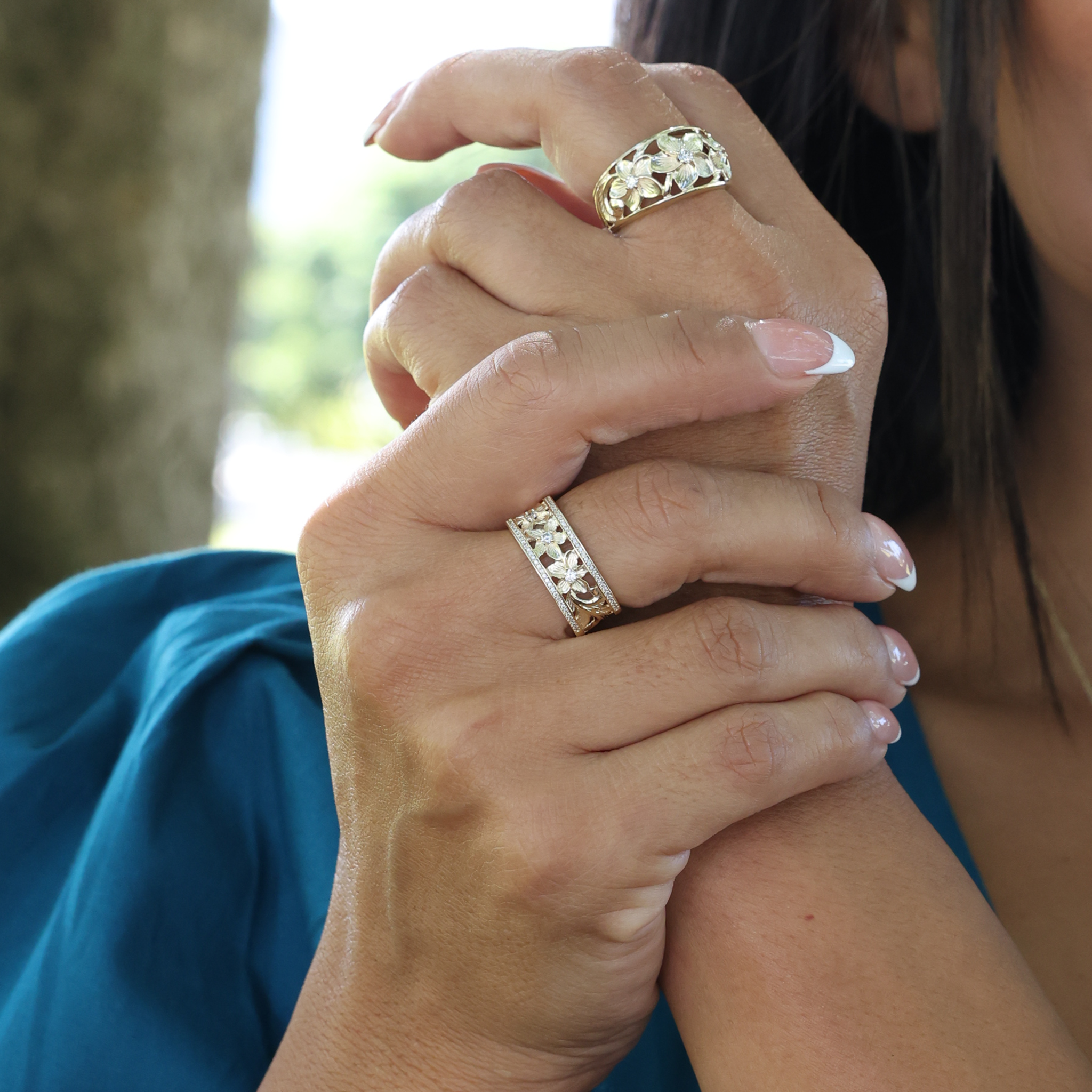 Woman's hands wearing two Hawaiian Heirloom Plumeria Rings in Gold with Diamonds
