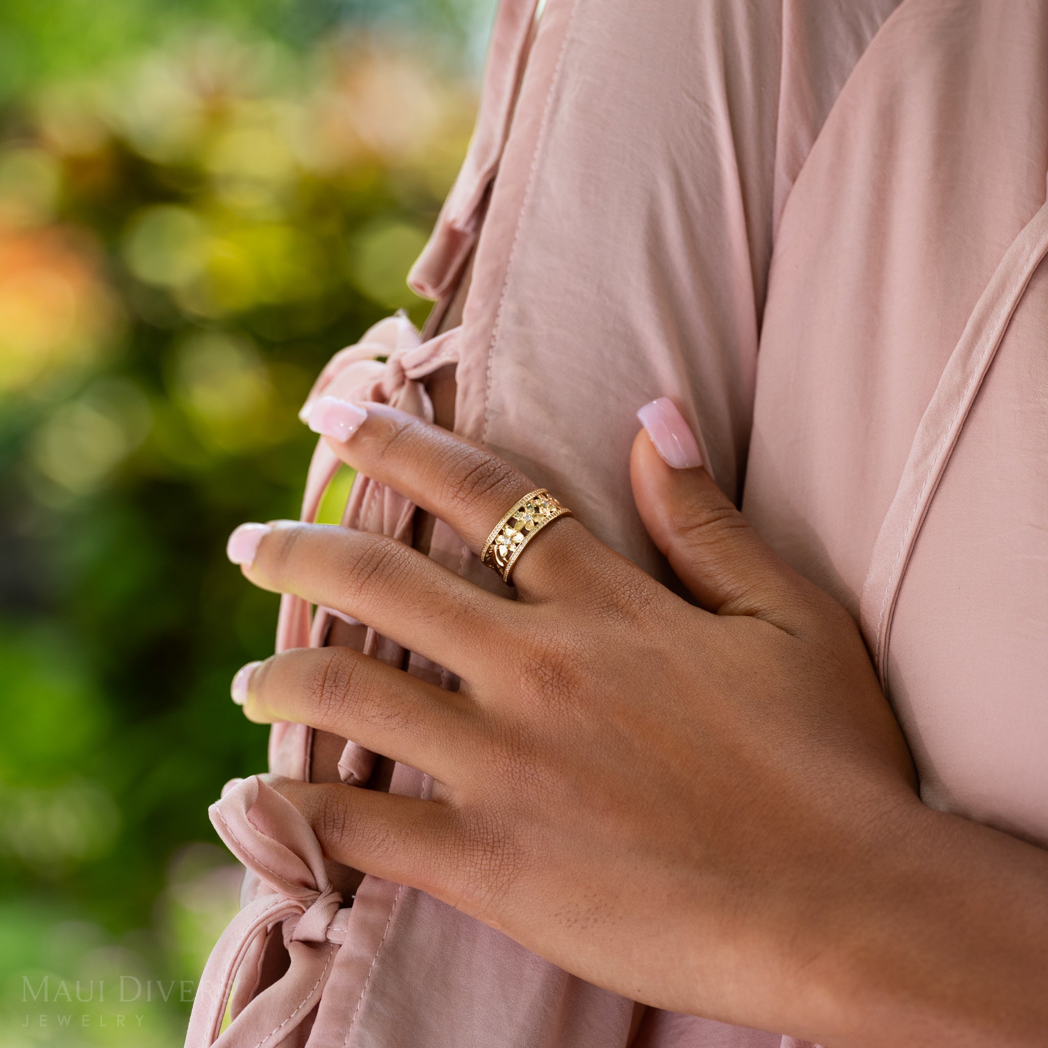 Close-up of a hand wearing a Hawaiian Heirloom Plumeria Ring in Gold with Diamonds on a natural background