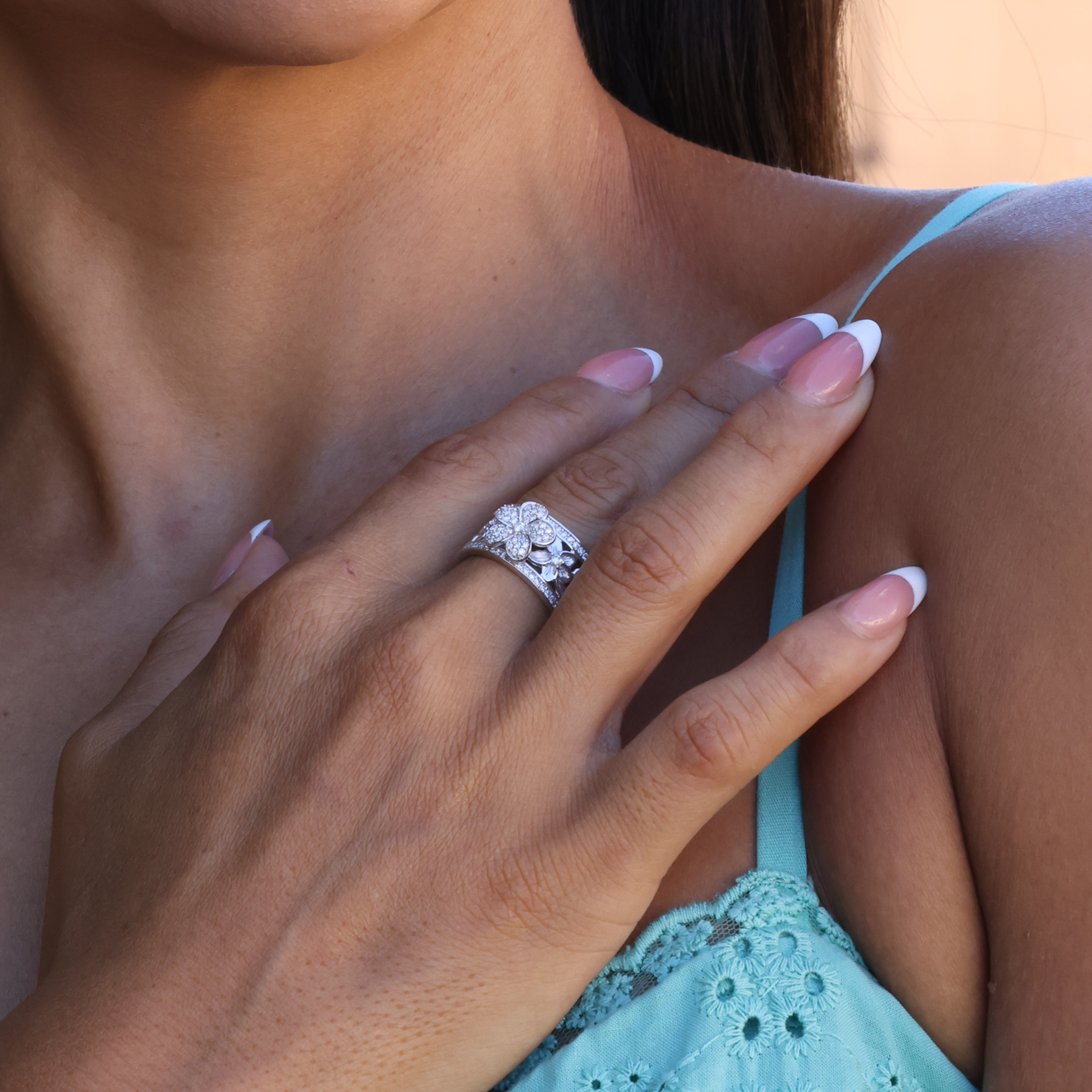Hawaiian Heirloom Plumeria Ring in White Gold with Diamonds on Hand touching shoulder over teal shirt