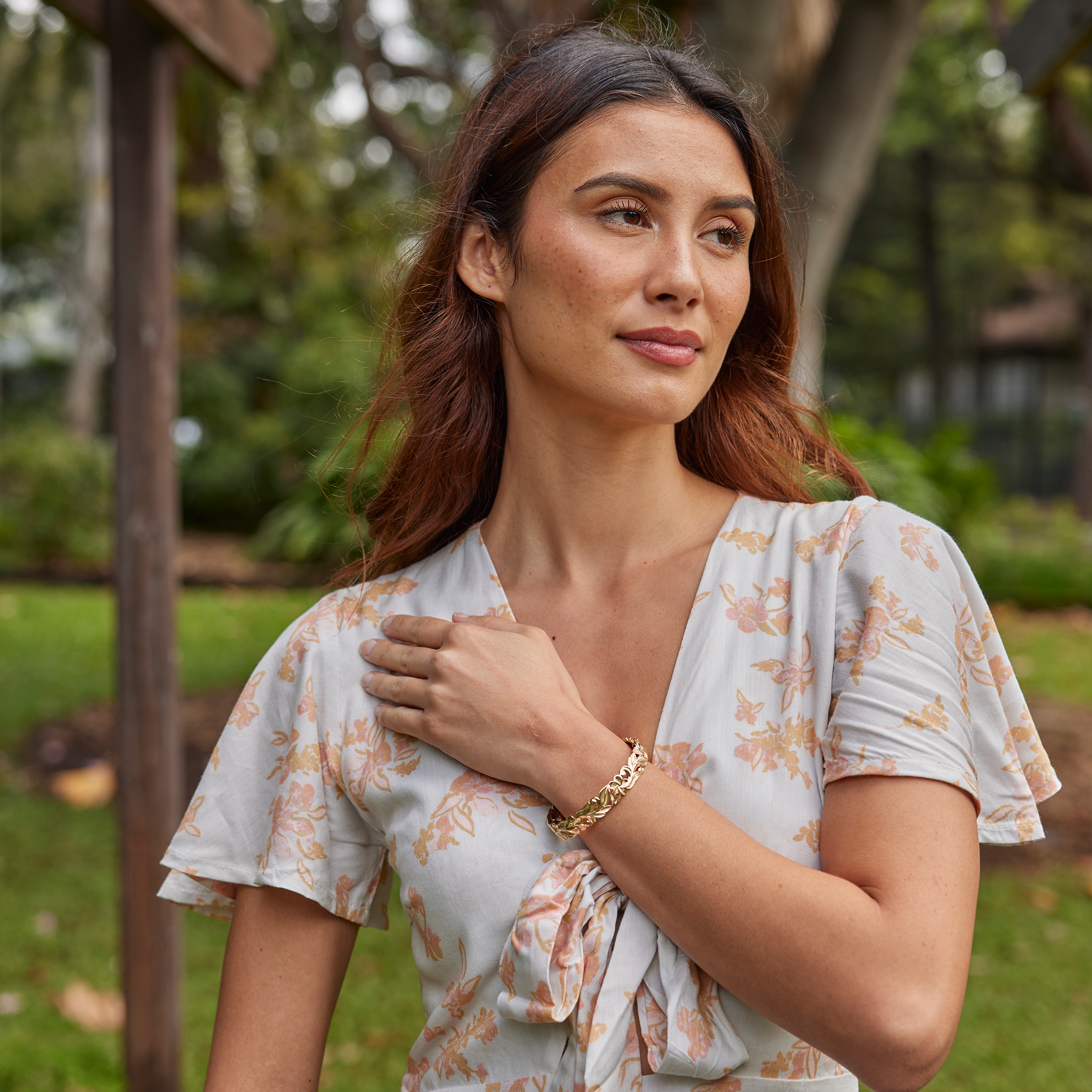 Woman in a park wearing a Hawaiian Heirloom Plumeria Hinge Bracelet in Gold
