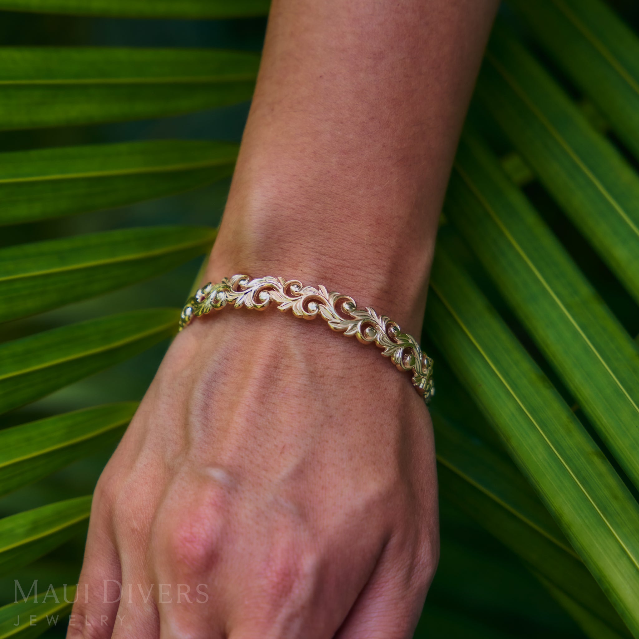 Living Heirloom Hinge Bracelet in 14k Yellow Gold on a wrist with a green leafy background