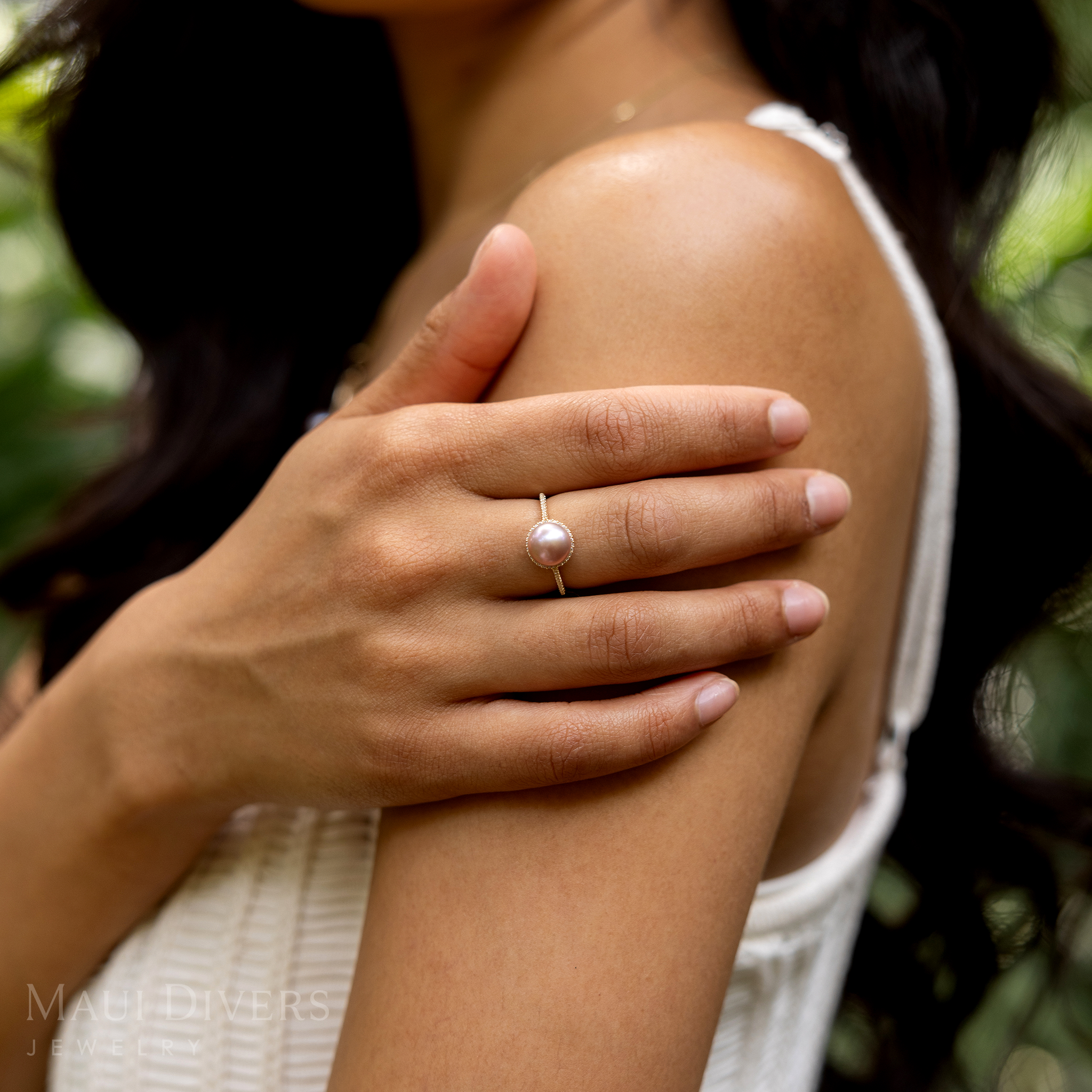 Woman's hand wearing a Pick A Pearl Halo Ring in Gold with Diamonds and Lavender Pearl in a garden