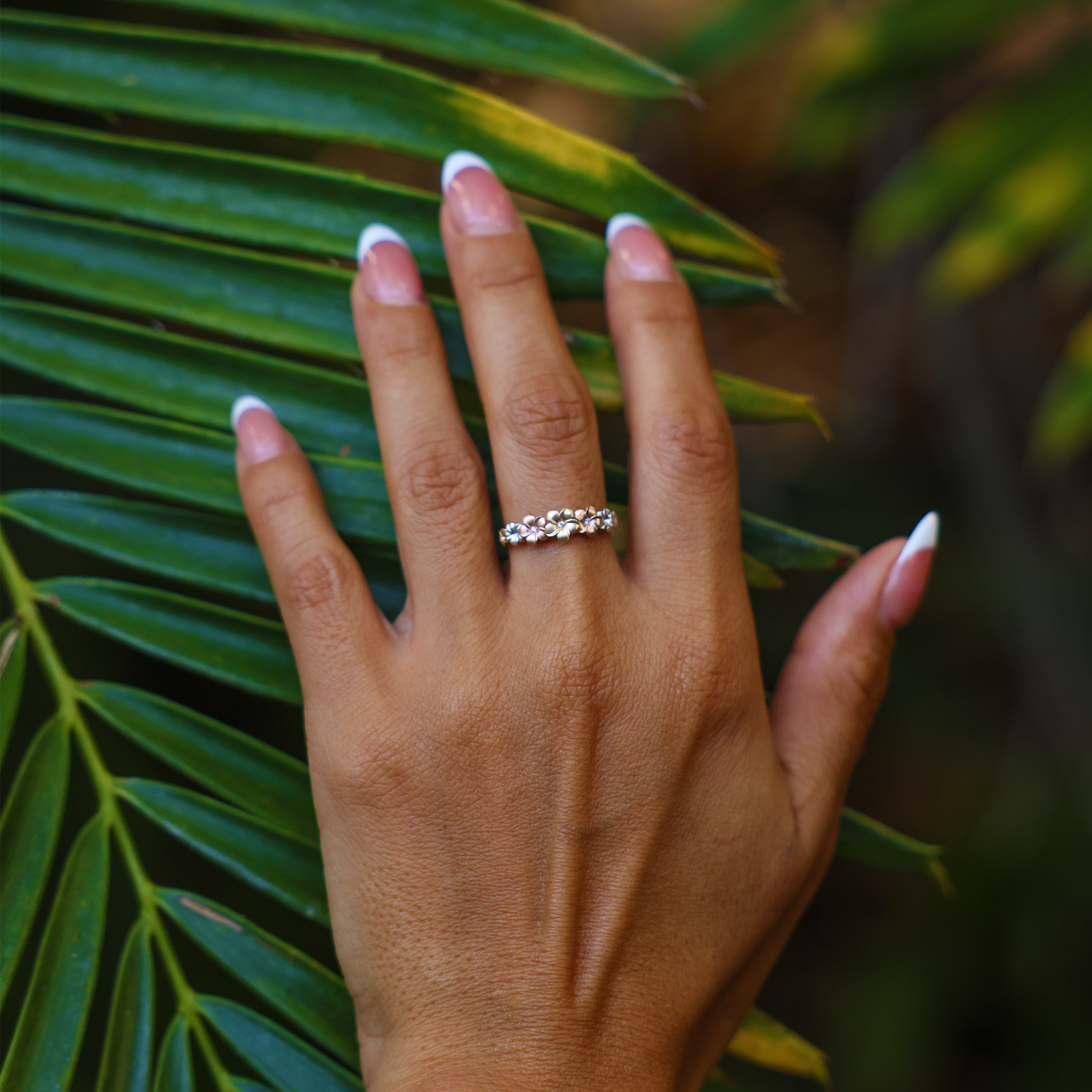 6mm 7-Plumeria Ring in Tri Color Gold with Diamonds on a hand over a palm leaf