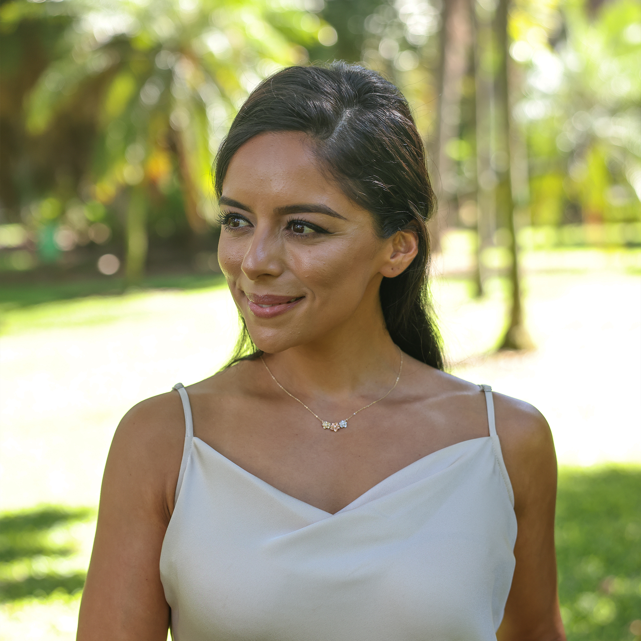 Woman in a garden wearing a 16" Three Plumeria Necklace in Tri Color Gold with Diamonds