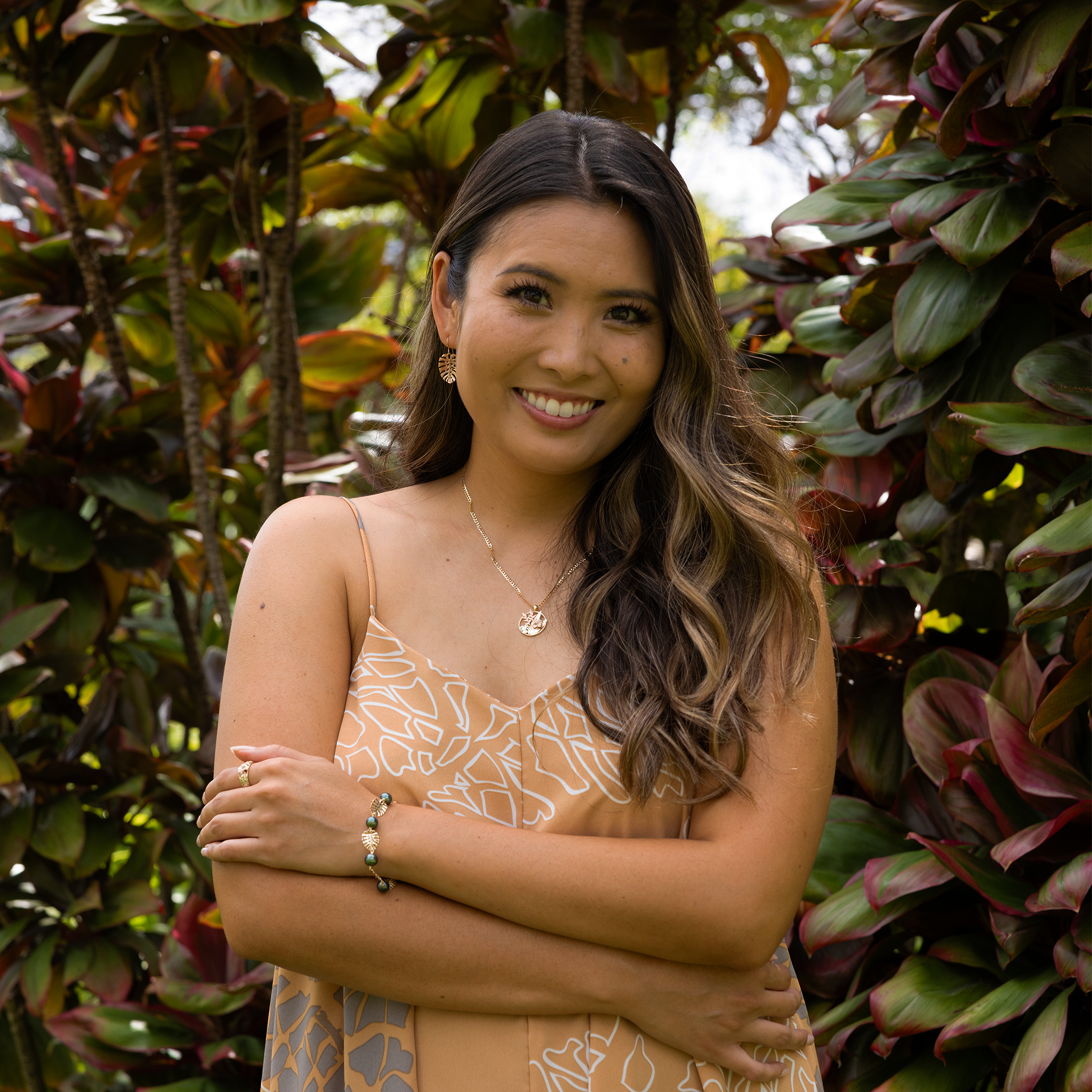 Woman in a tropical garden wearing 23mm Monstera Earrings in Gold and Monstera Pearl Bracelet