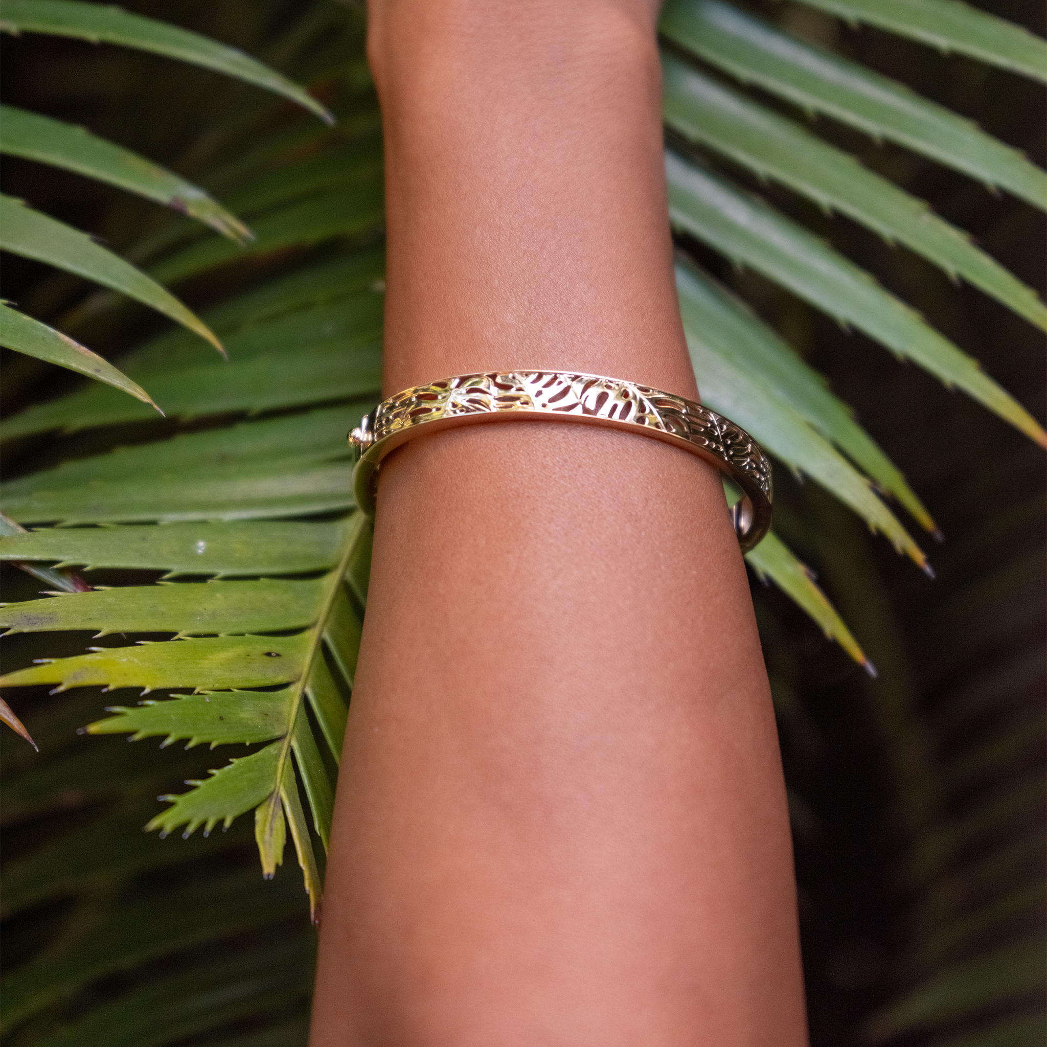 Close up an 8mm Monstera Hinge Bracelet in Gold on wrist with leafy green in the background
