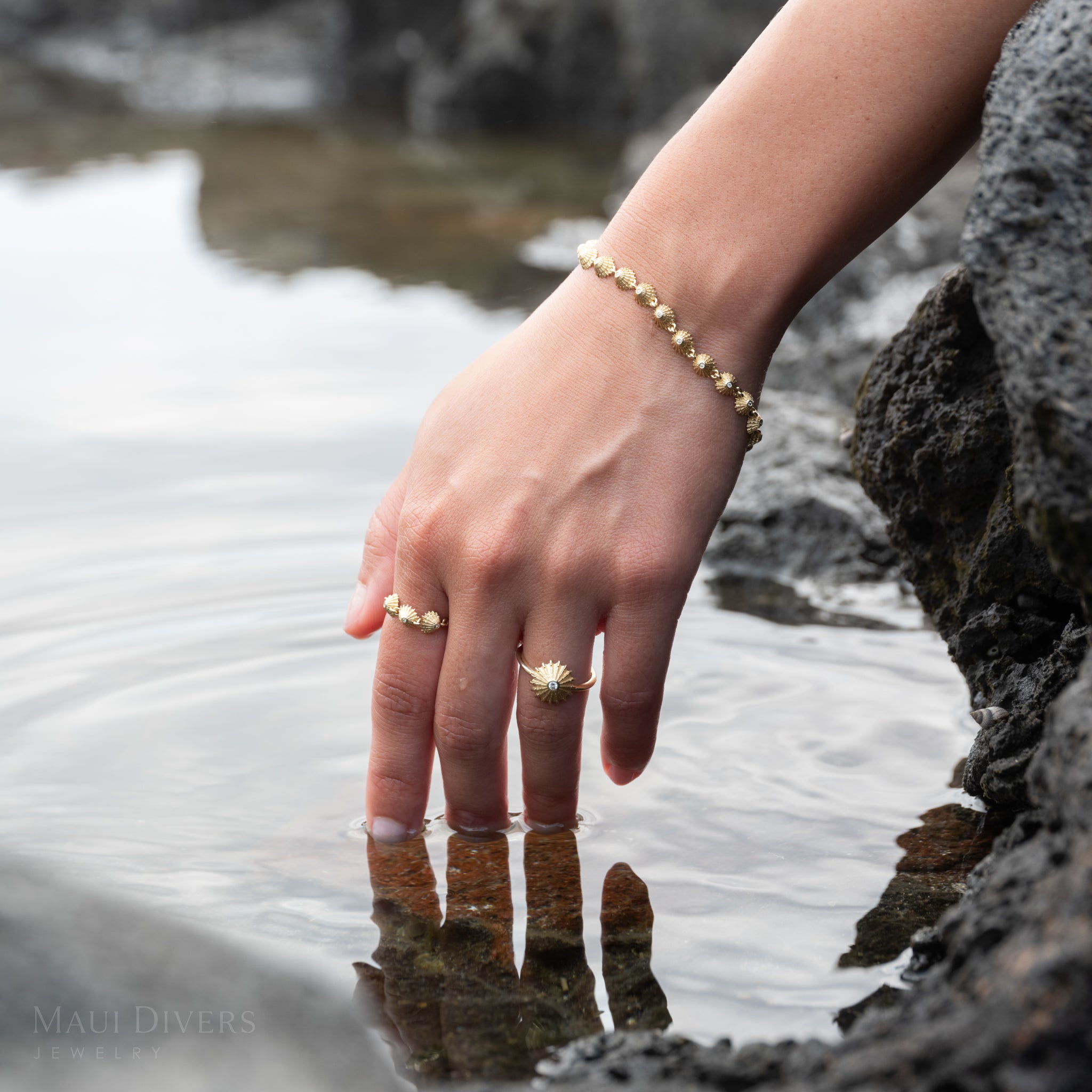 Close-up of a hand reaching into water wearing gold and diamond ʻopihi rings and a gold and diamond ʻopihi bracelet