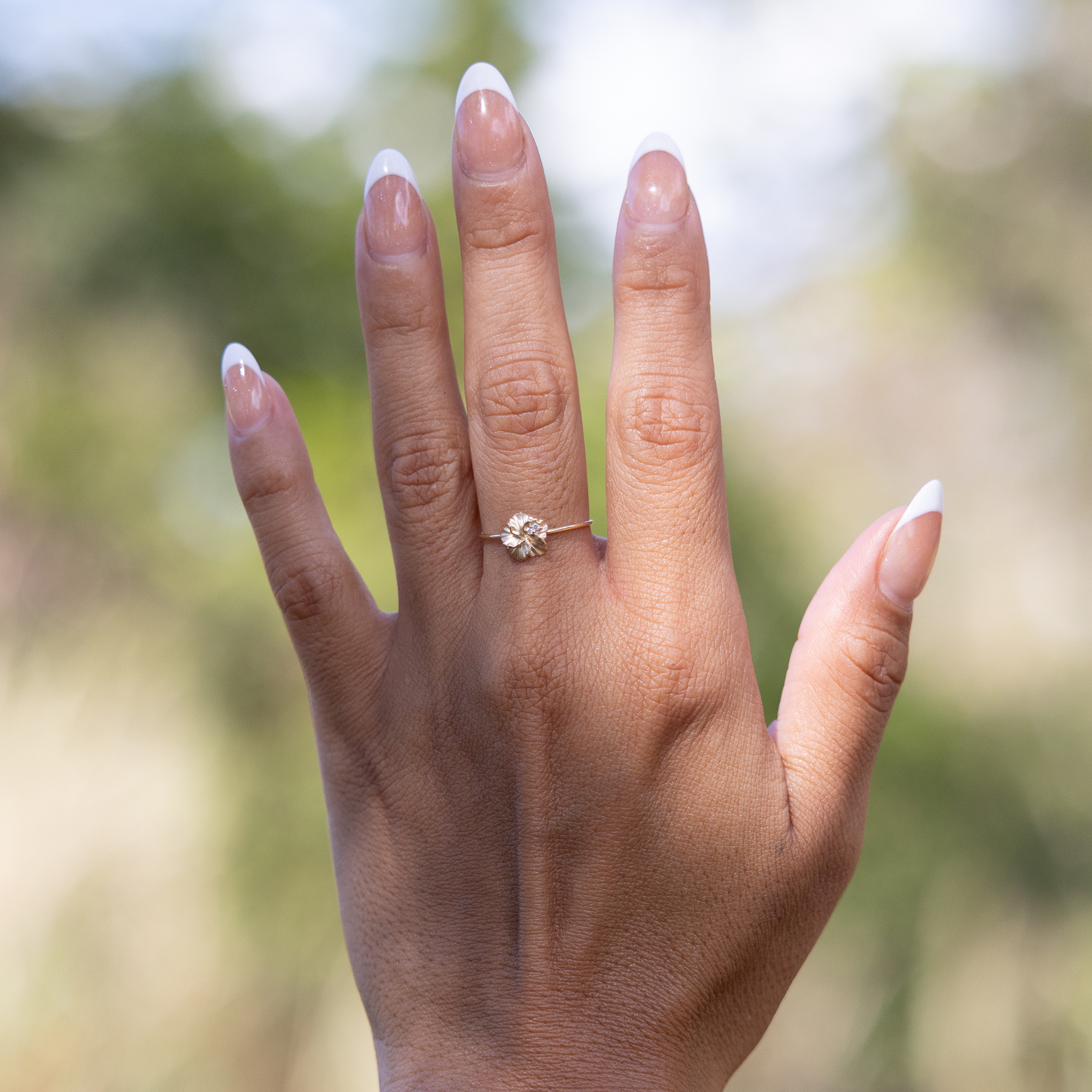 8mm Hawaiian Gardens Hibiscus Ring in 14k Yellow Gold with Diamonds on hand held up against blurred nature background