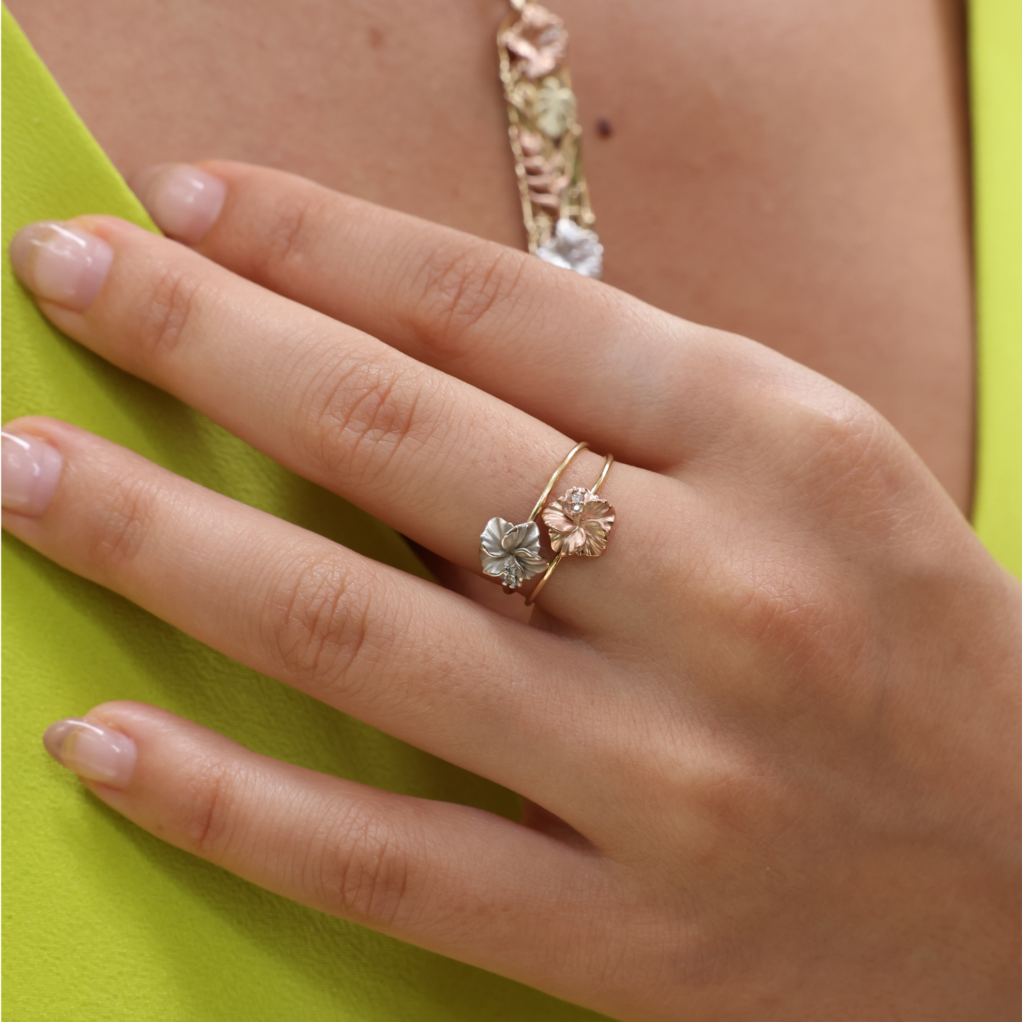 Close up of two Hawaiian Gardens Hibiscus Rings in Gold with Diamonds on a womanʻs hand