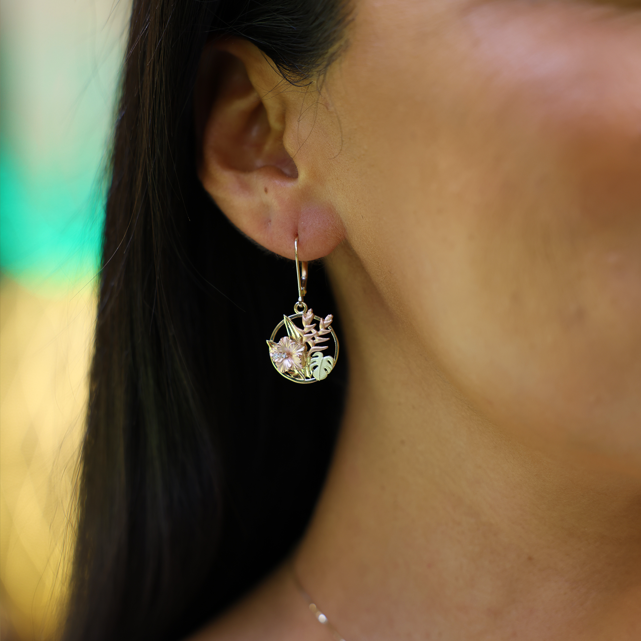A woman's ear with Hawaiian Gardens Hibiscus Earrings in Tri Color Gold with Diamonds