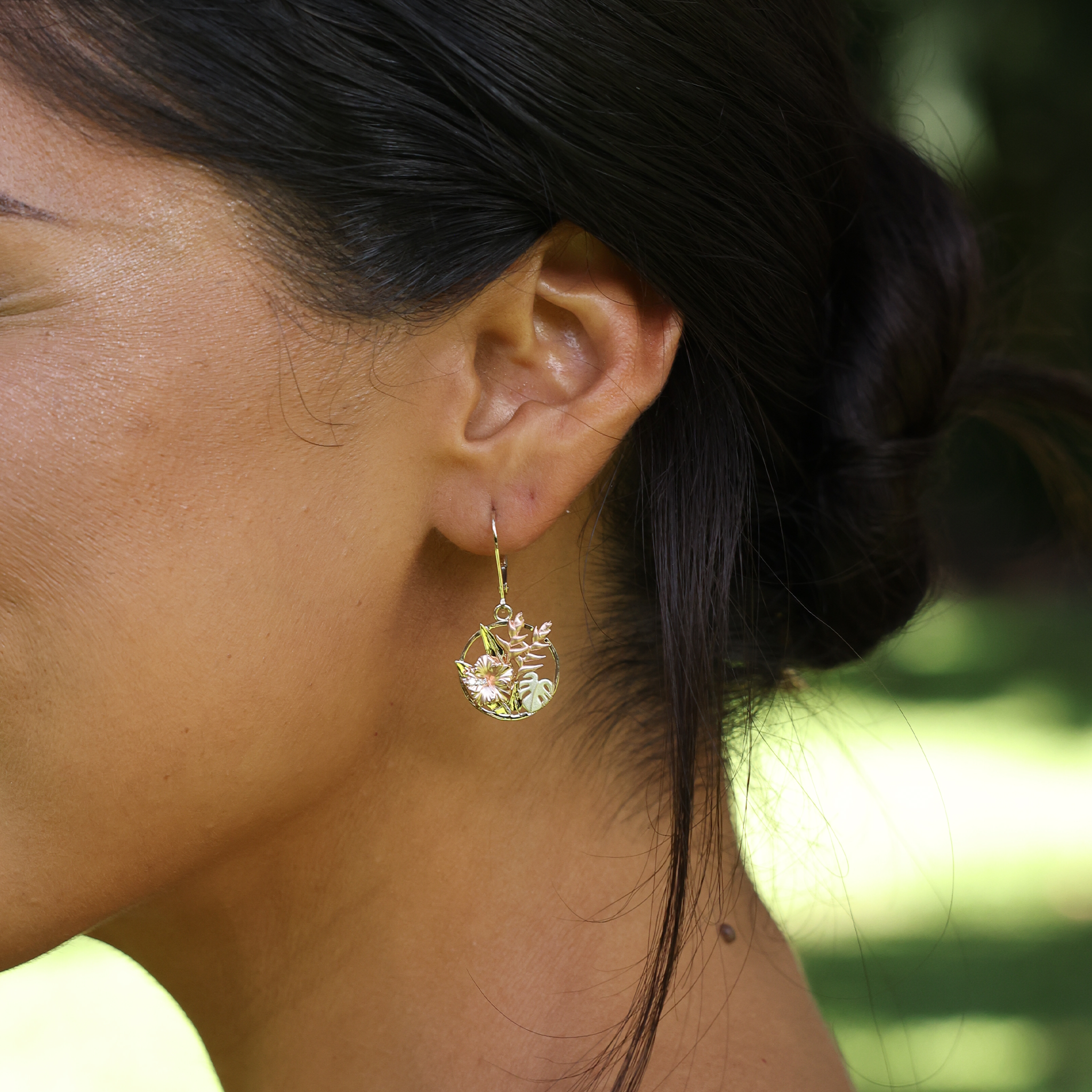 Close up of Hawaiian Gardens Hibiscus Earrings in Tri Color Gold with Diamonds on ear with blurred nature background