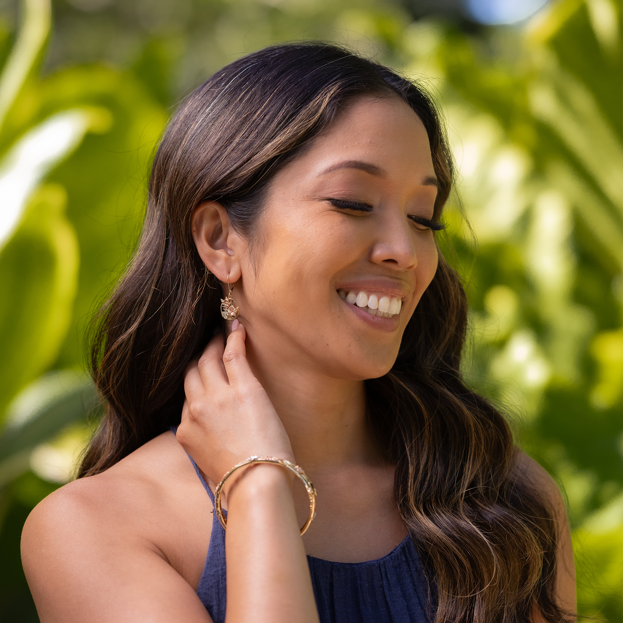 Woman in a garden wearing Hawaiian Gardens Hibiscus Earrings and Bracelet in Tri Color Gold with Diamonds