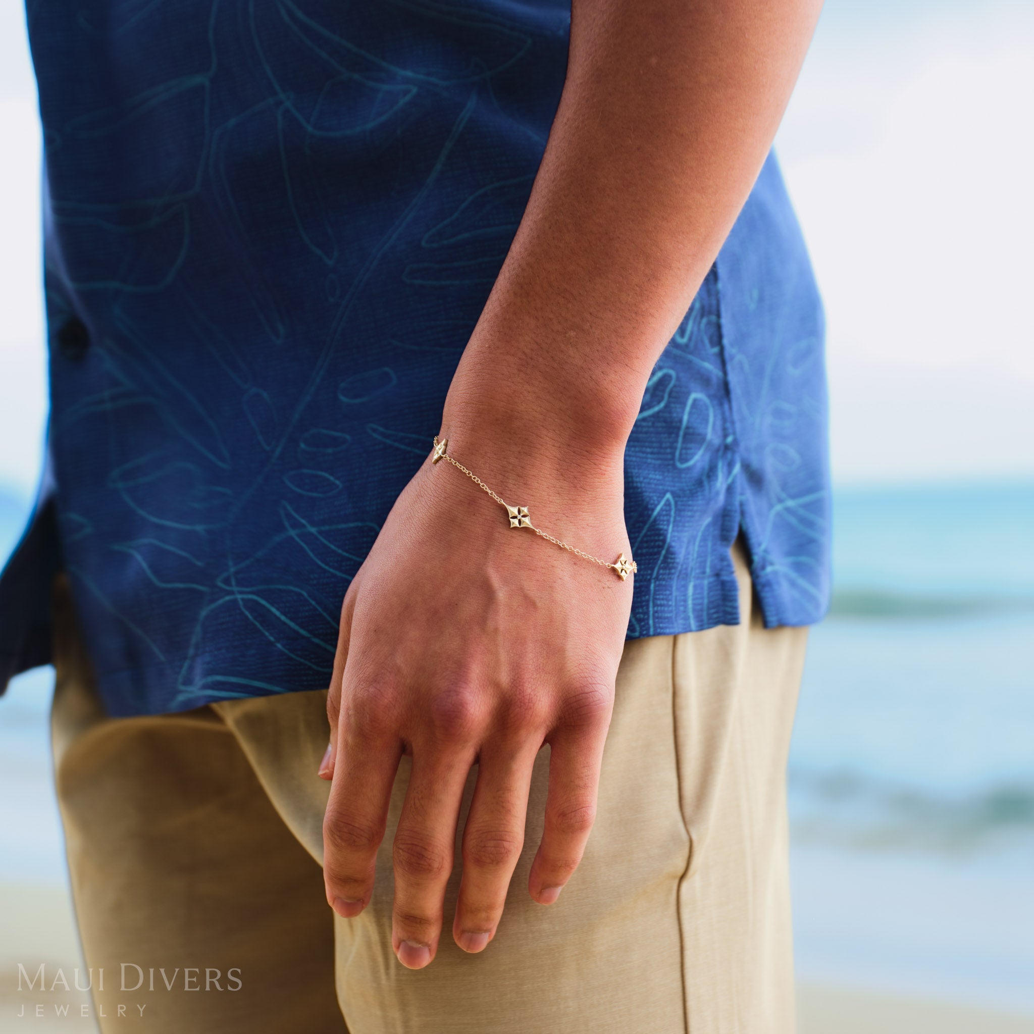 Person wearing a Hawaiian Quilted Star Bracelet in Gold with Diamonds on a blurred beach background