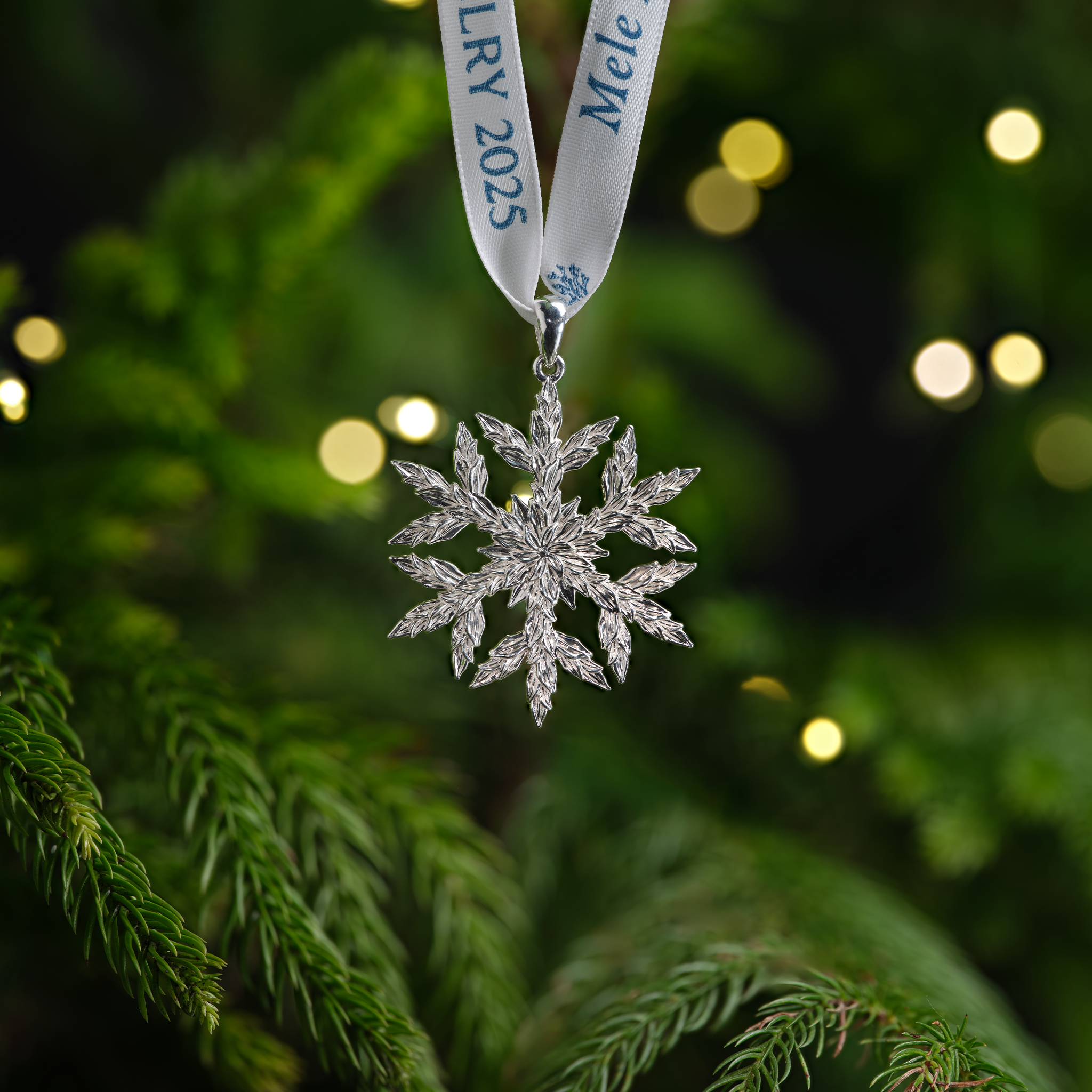 Silver Hawaiian snowflake ornament on a ribbon, hanging on a Christmas tree.