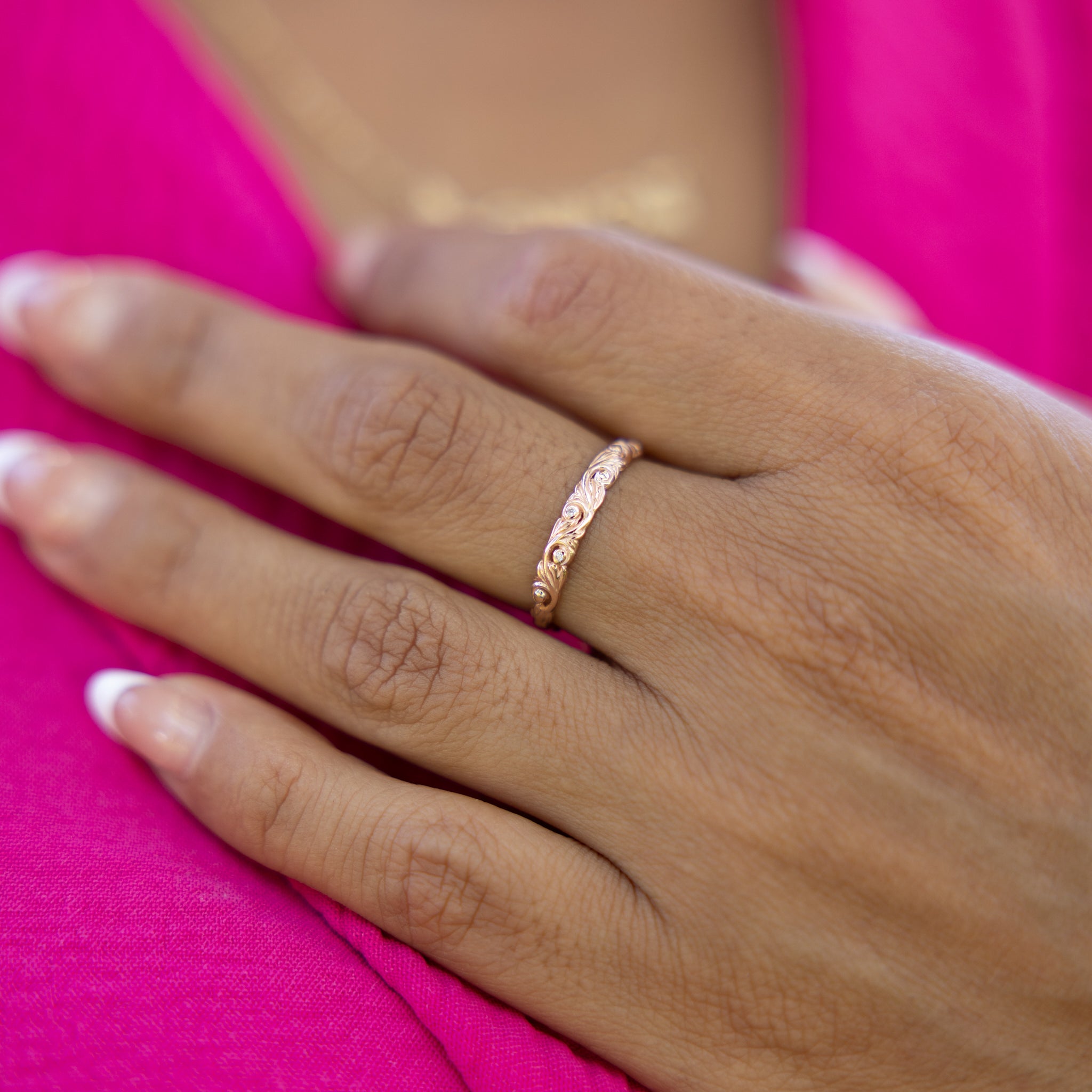 A woman's hand wearing a Living Heirloom Ring in Rose Gold with Diamonds resting on a pink top