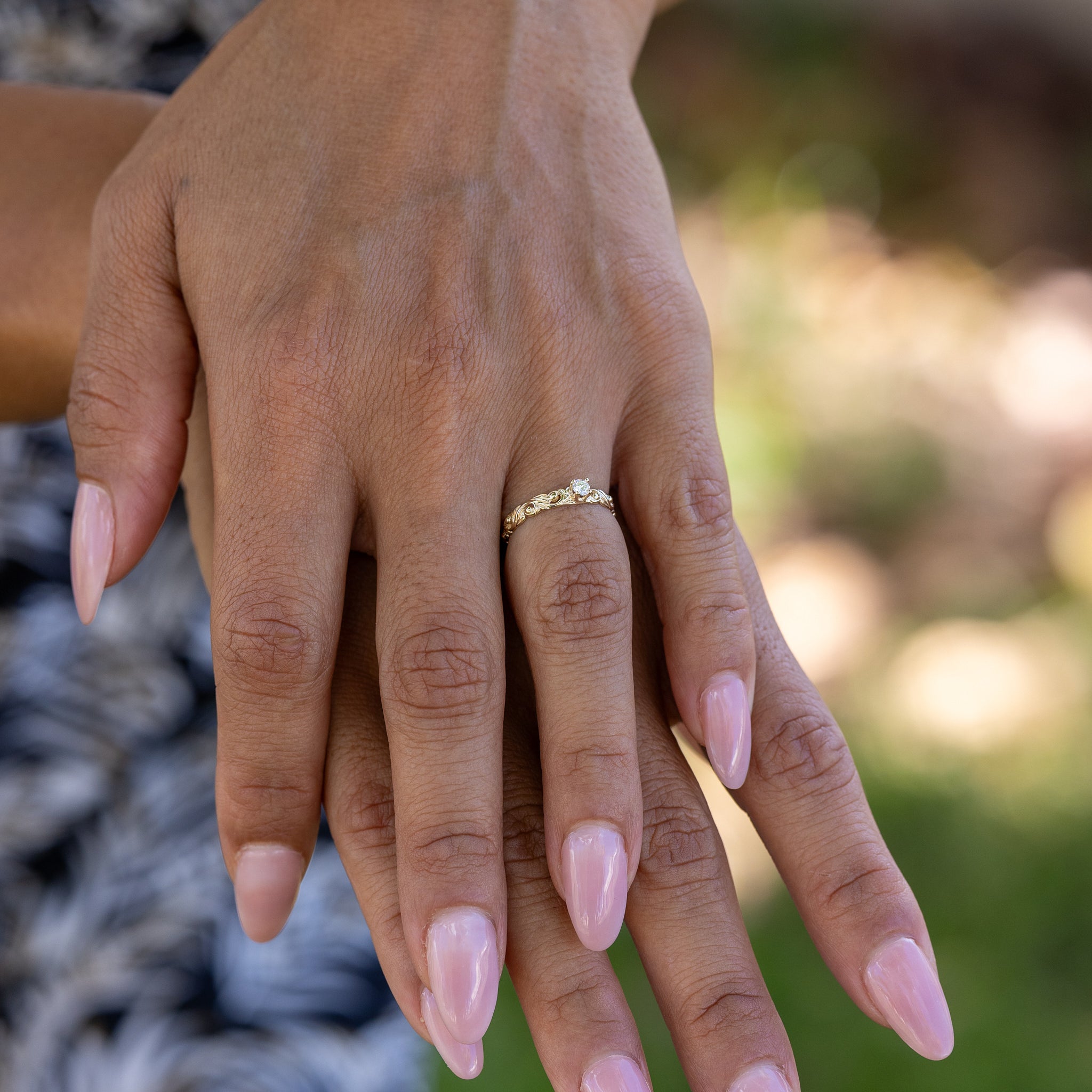 Close-up of Living Heirloom Ring in 14k Yellow Gold with Diamond on a woman's hands with blurry green background