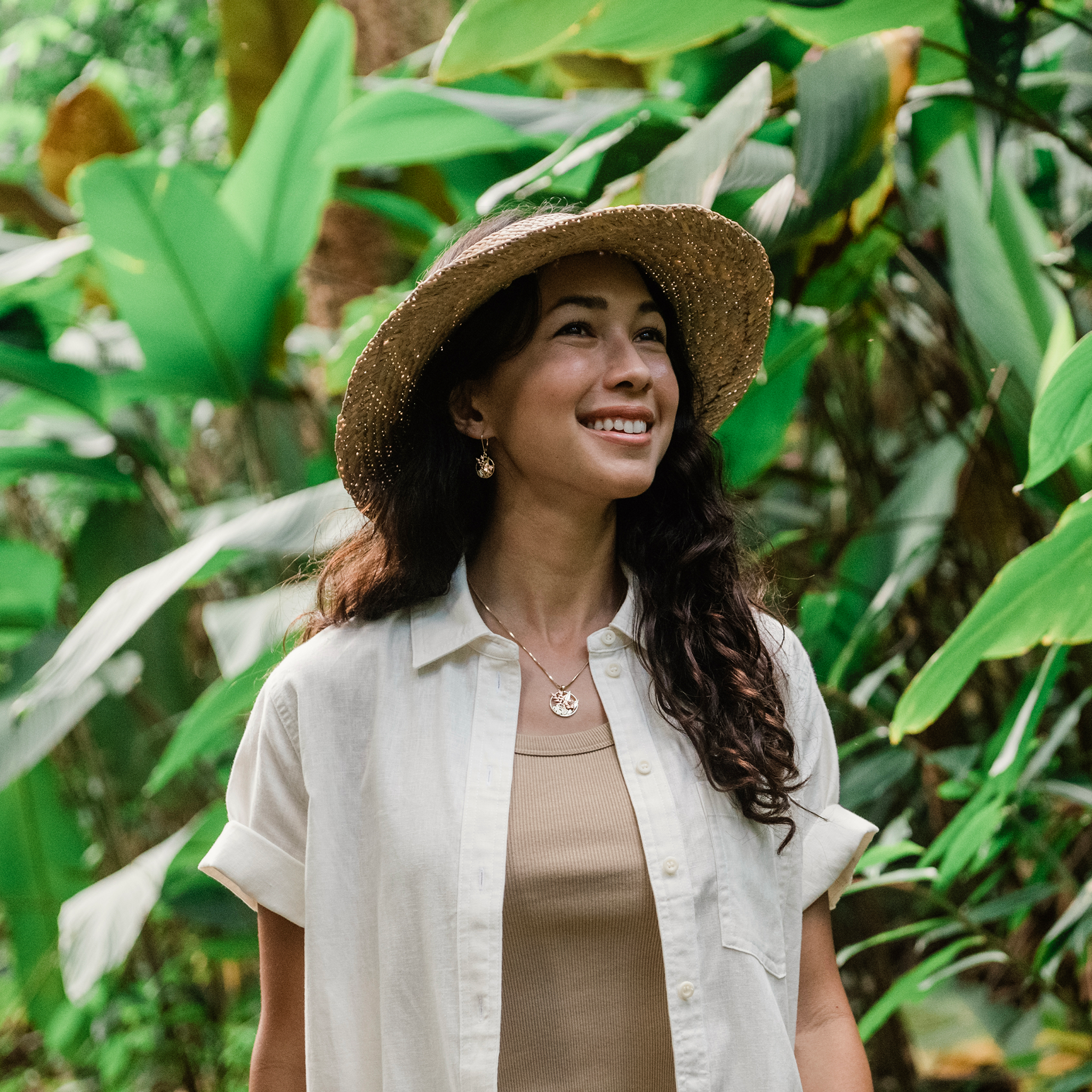 Woman in a tropical forest wearing Hawaiian Gardens Hibiscus Earrings and Pendant in Tri Color Gold with Diamonds